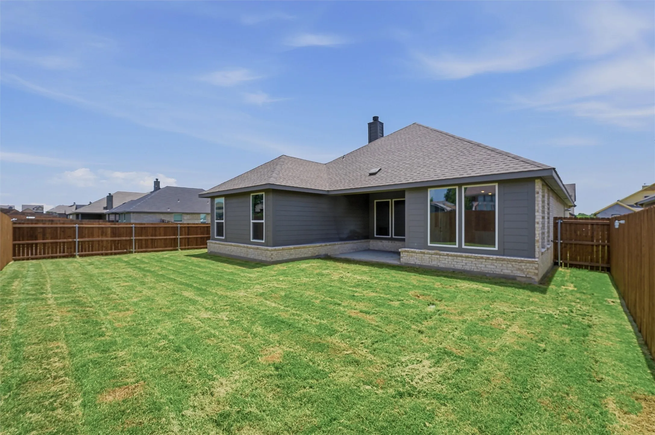 Spacious backyard featuring a privacy fence, an exterior with gray siding and stone accents, a concrete patio, and multiple windows