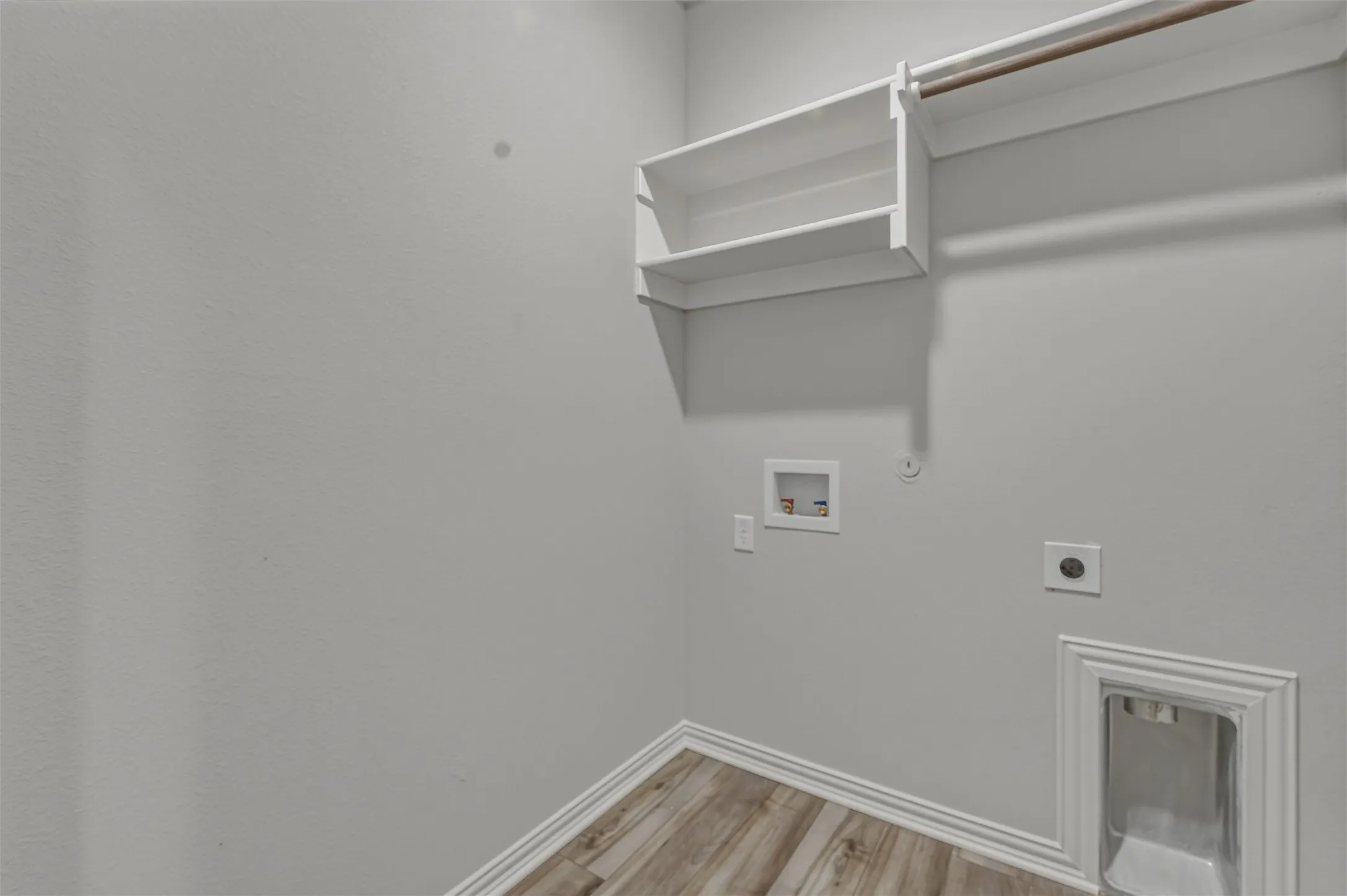 Utility area featuring wood-finish flooring, white baseboards, light gray walls, built-in shelving, and a garment rod