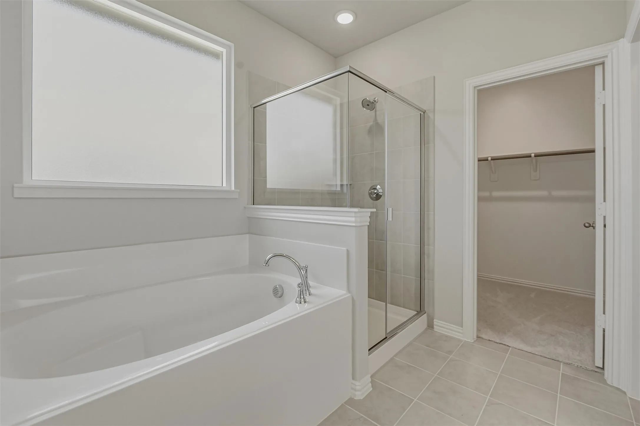 Bathroom featuring a built-in soaking tub with chrome fixtures, a glass-enclosed shower with tile surround, and light-toned tile flooring