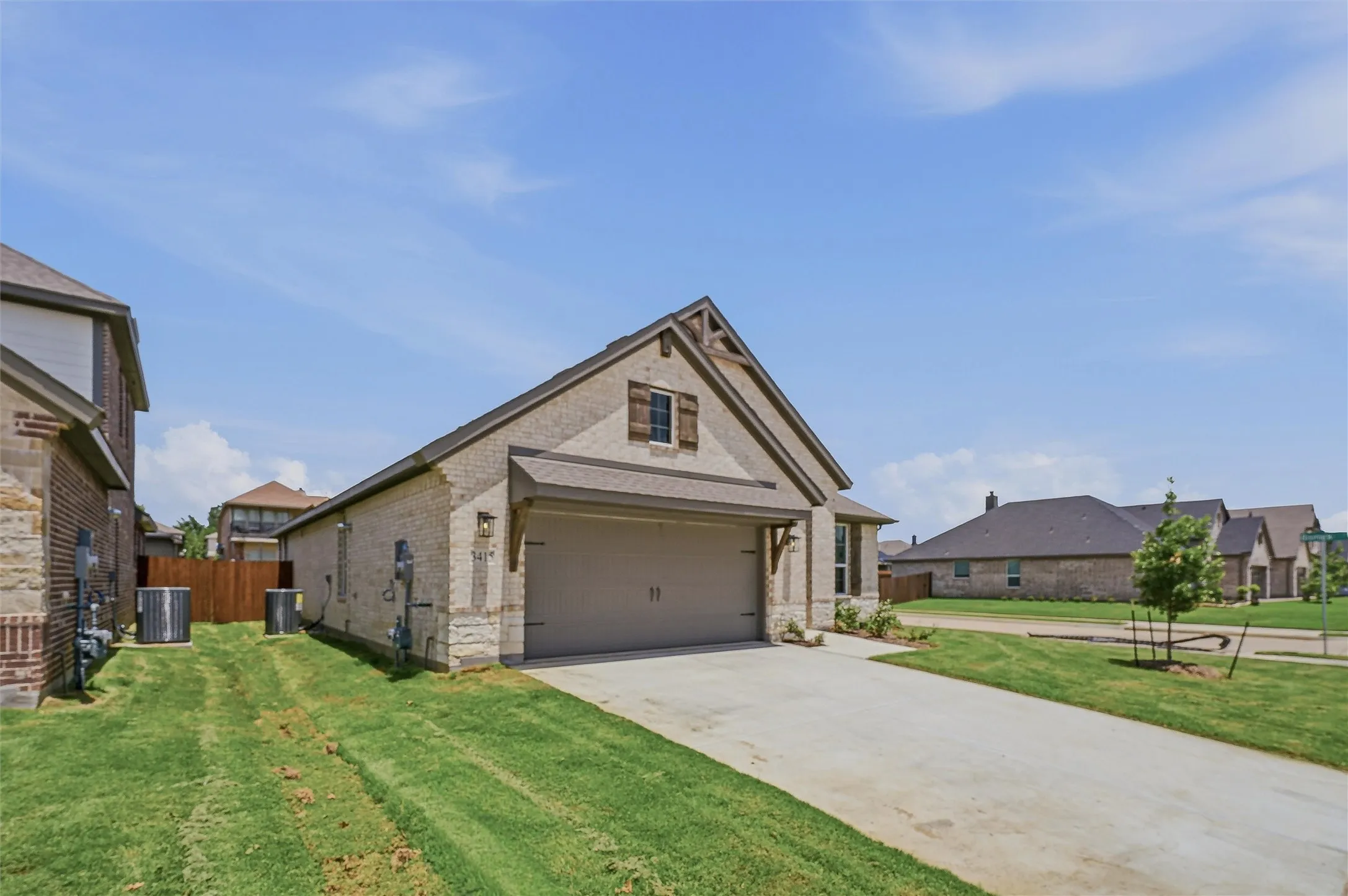 Exterior featuring a brick and stone facade, a two-car garage with a wood-look door, a concrete driveway, and a gabled roofline with decorative wood accents