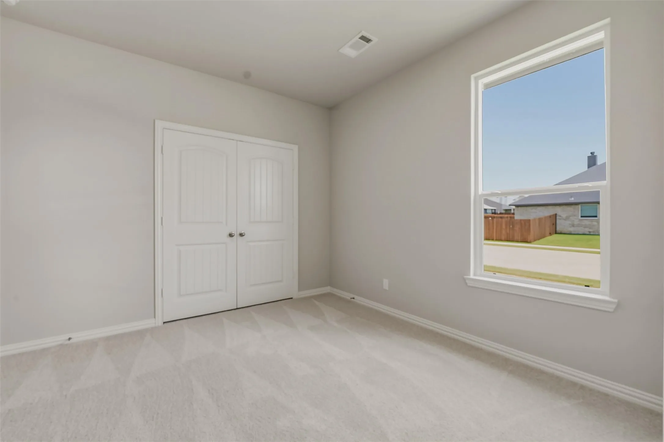 Spacious room featuring light gray walls, plush patterned carpeting, and white trim