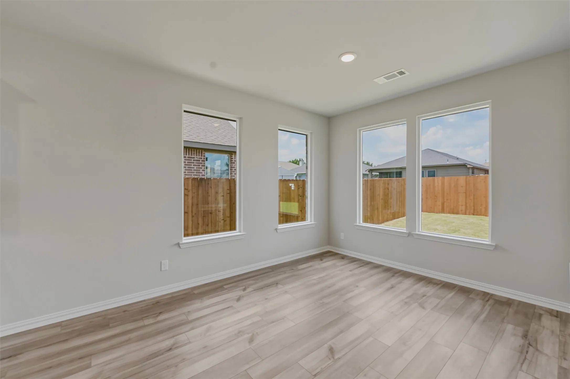 Spacious room featuring multiple windows, wood-finish flooring, recessed lighting, and light gray wall paint