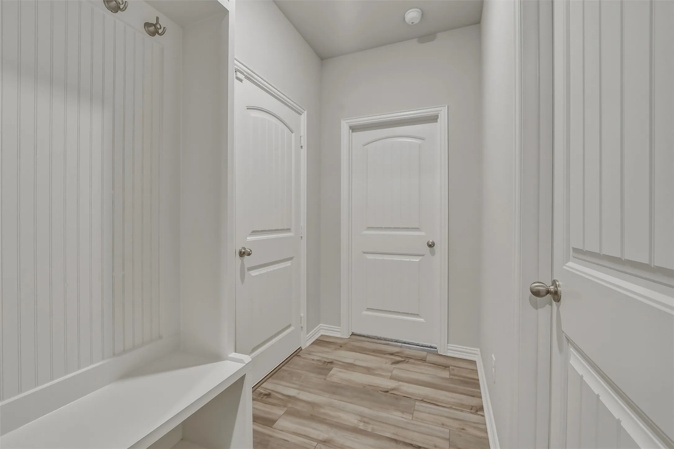 Entryway featuring built-in white cabinetry with hooks and shelving, light wood-finish flooring, and white paneled doors with satin nickel hardware