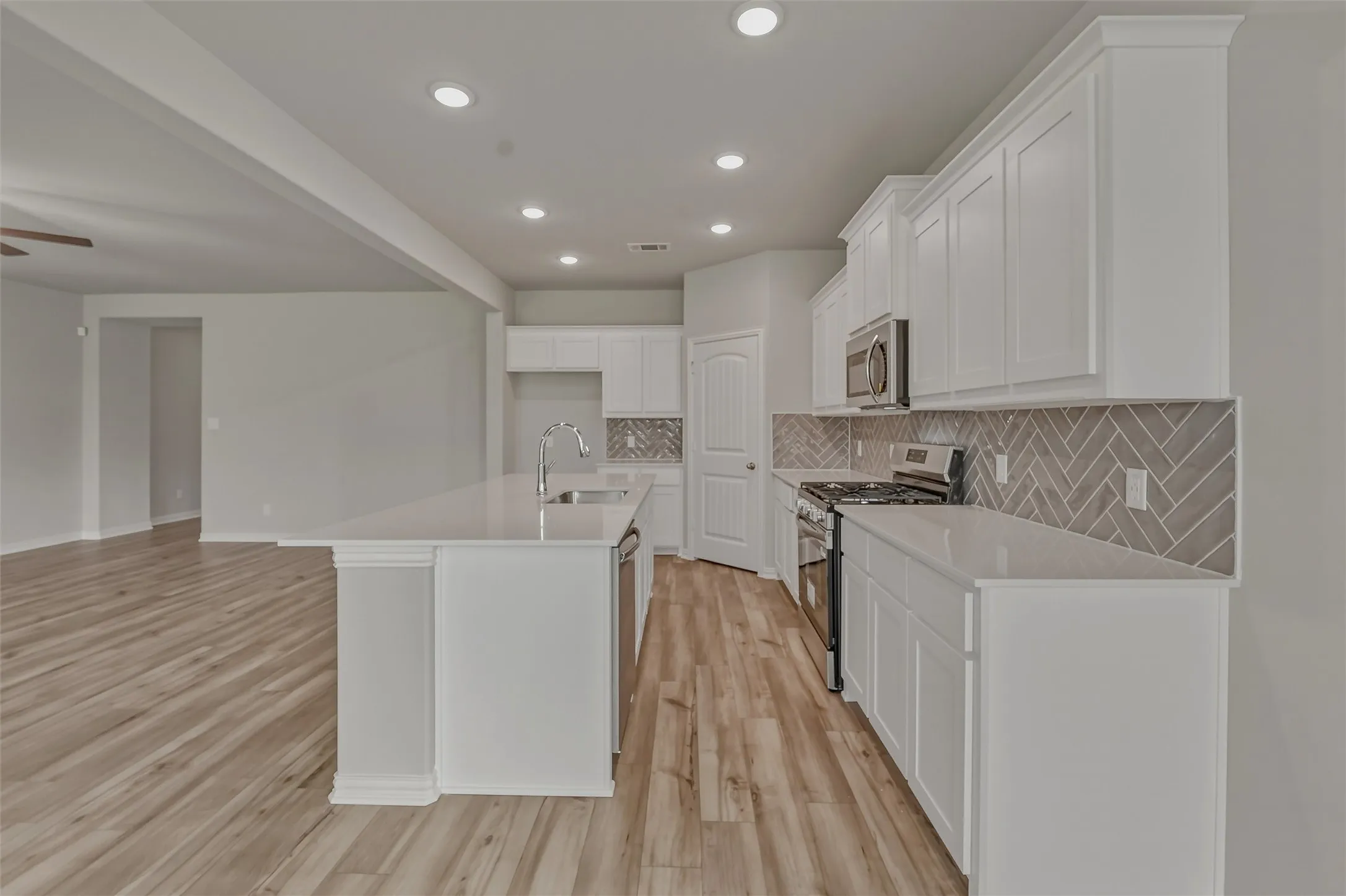 Modern kitchen featuring white shaker cabinetry, stainless steel appliances, a herringbone tile backsplash, an island with an undermount sink, and recessed lighting
