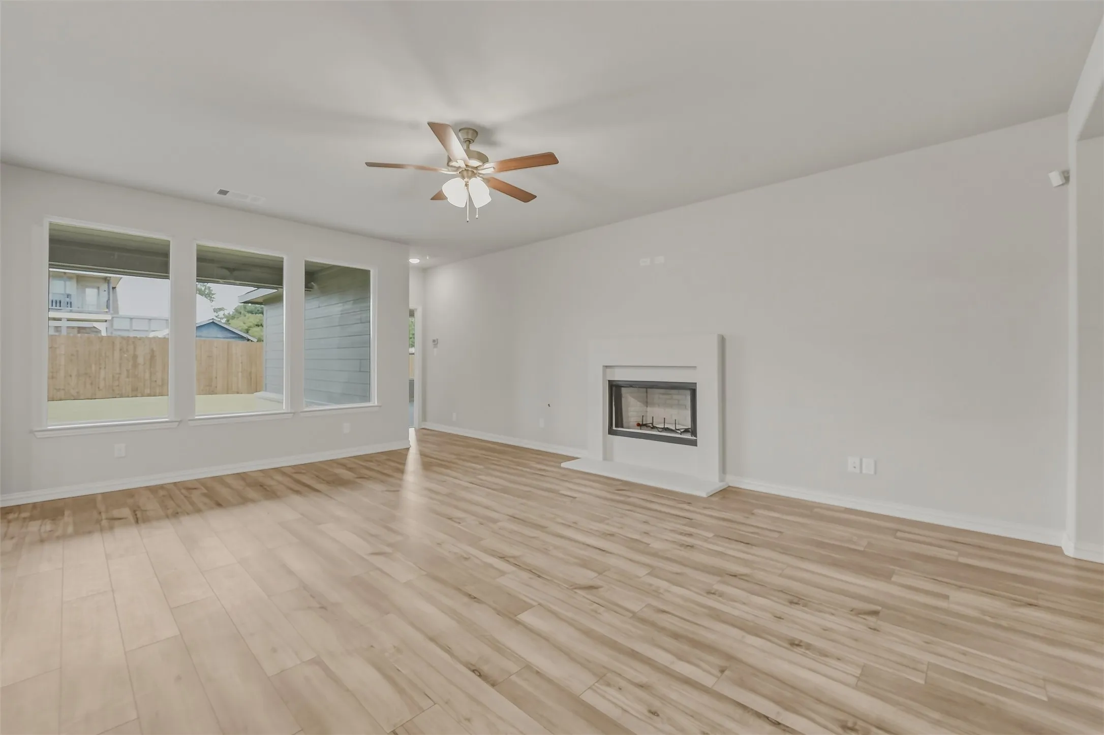 Spacious living area featuring wood-finish flooring, a contemporary fireplace with a white mantel, and a ceiling fan