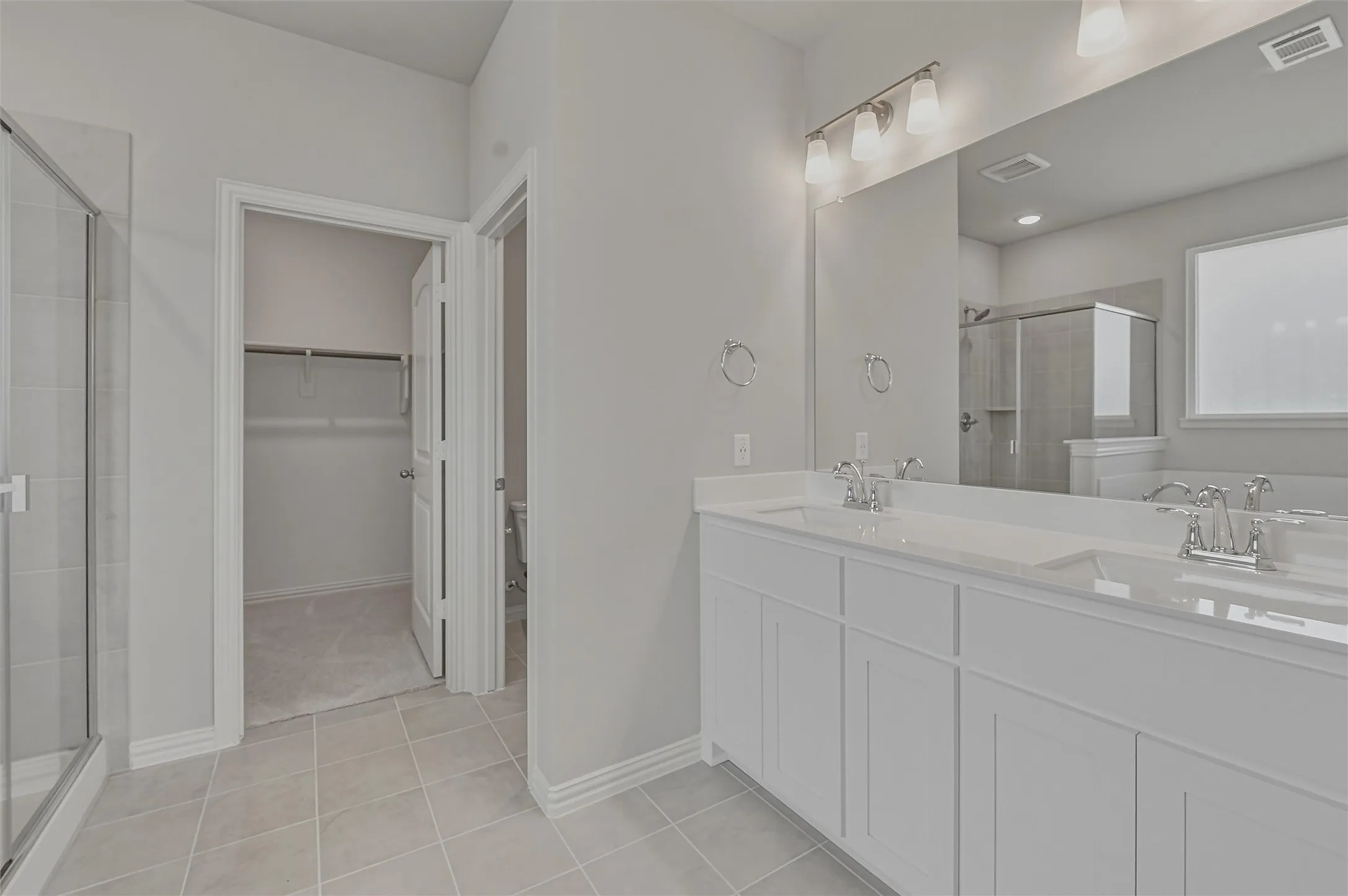 Bathroom featuring a dual vanity with white cabinetry and integrated sinks, a large mirror, and tiled flooring