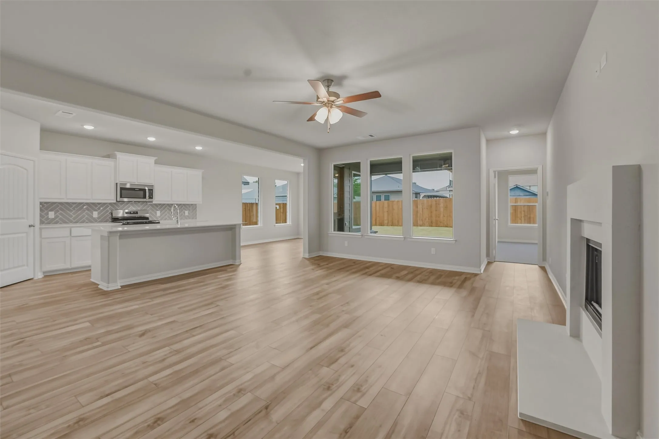 Open-concept living space featuring wood-finish flooring, a contemporary fireplace, and a kitchen with white cabinetry, stainless steel appliances, and a herringbone tile backsplash