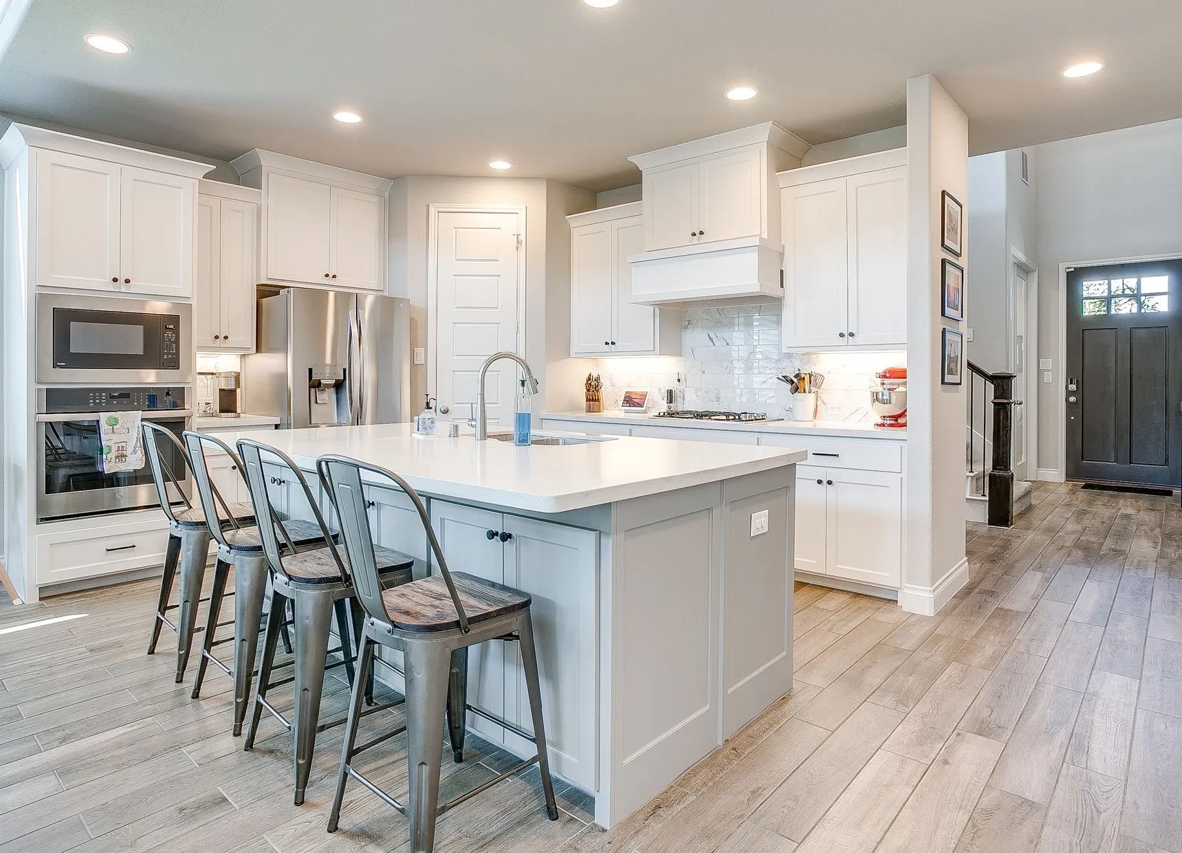 This gourmet kitchen is equipped with an oversized island with generous seating, stainless steel appliances, abundant cabinetry, quartz countertops, a marble backsplash, and a gas cooktop and oven.
