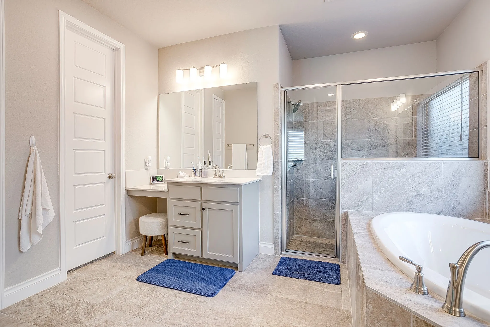 A spacious walk-in shower and a second vanity with a built-in seating area add both comfort and functionality to the space.
