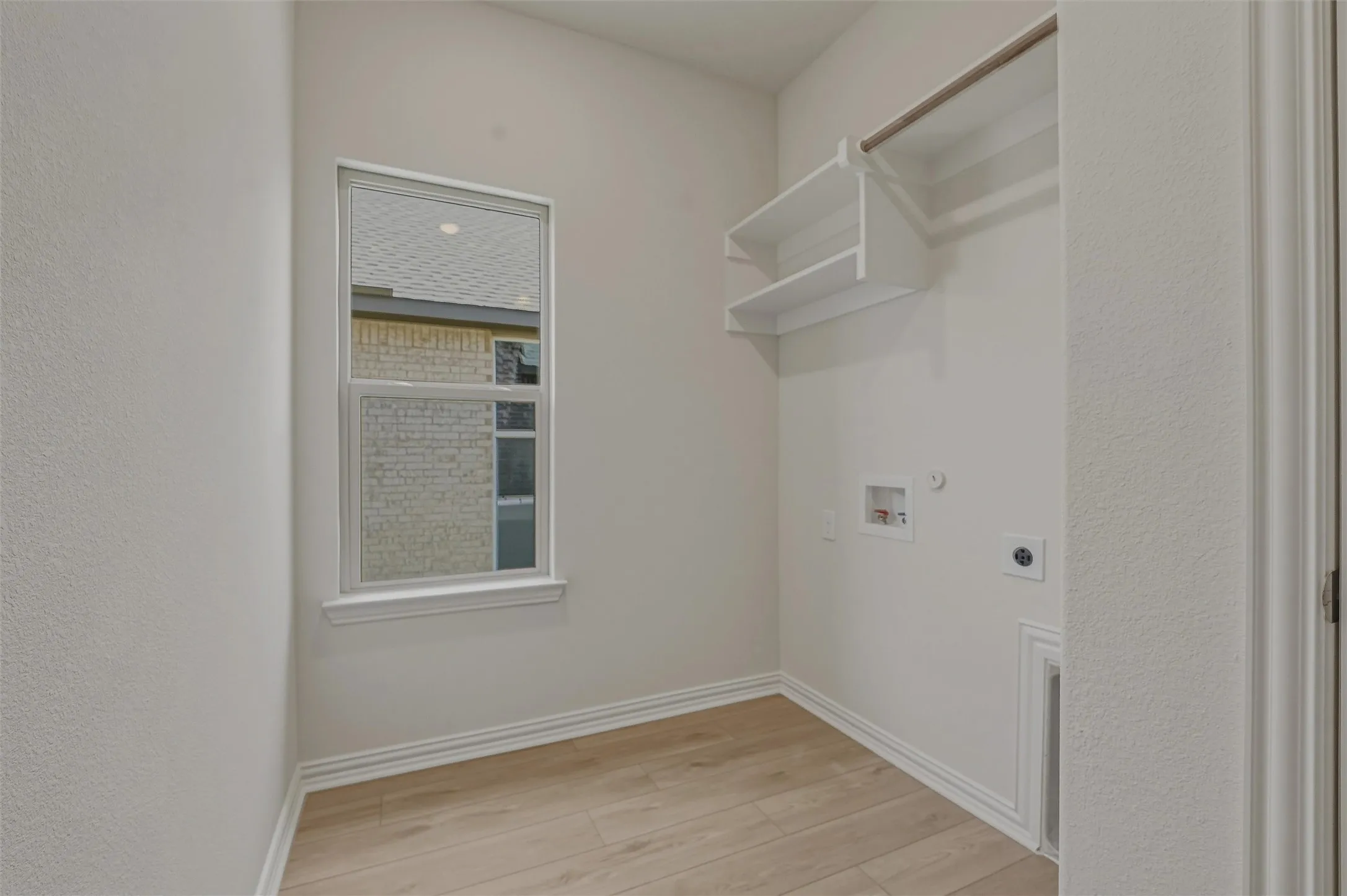 Dedicated laundry space featuring wood-finish flooring, a window for natural light, built-in shelving, a hanging rod, and utility hookups