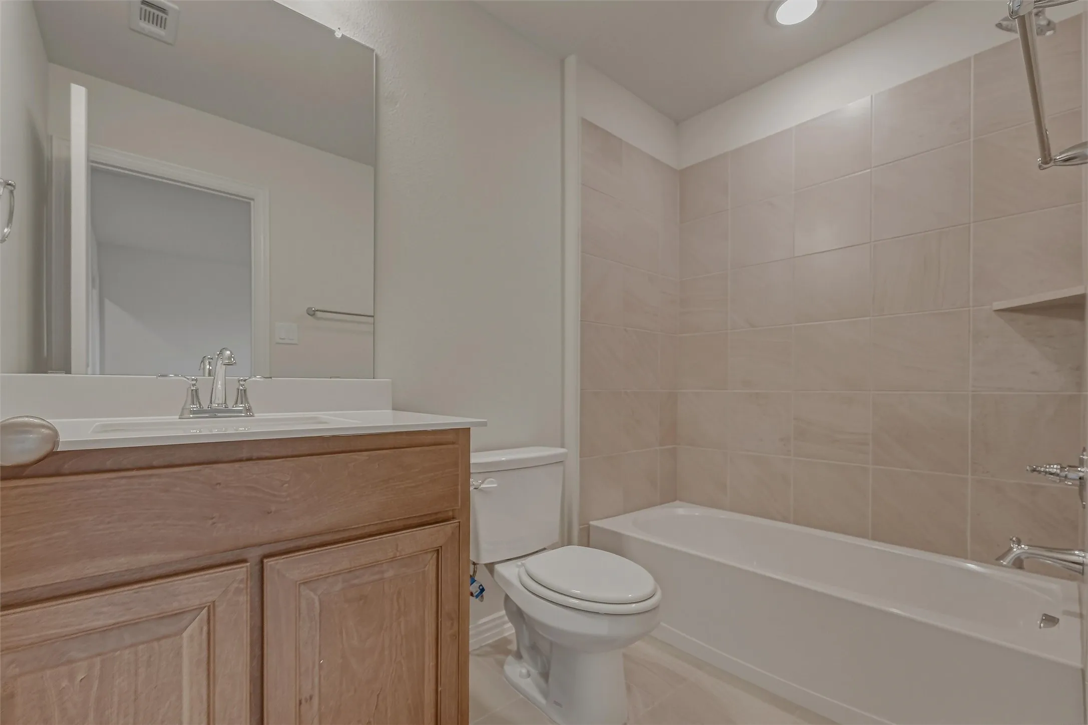 Bathroom featuring a wood-finish vanity with a single sink, an integrated mirror, a toilet, a bathtub with tiled surround, and recessed lighting