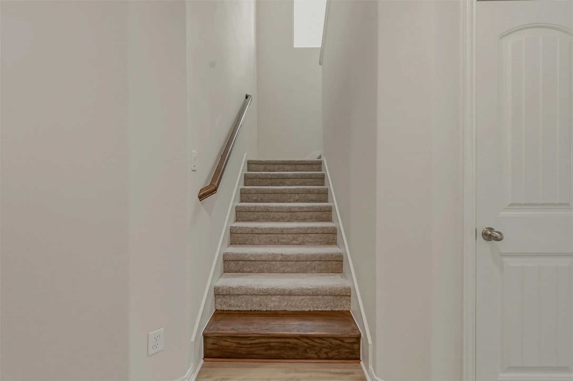 Carpeted staircase featuring a wood-finish bottom step and a contemporary handrail