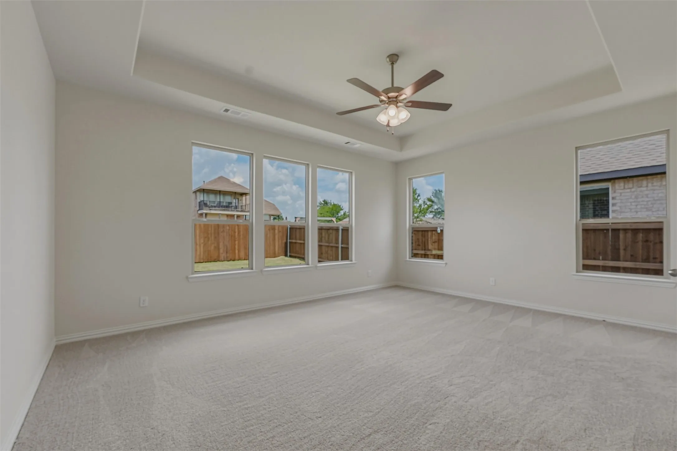 Spacious room featuring light gray carpet, multiple large windows, and a ceiling fan with integrated lighting