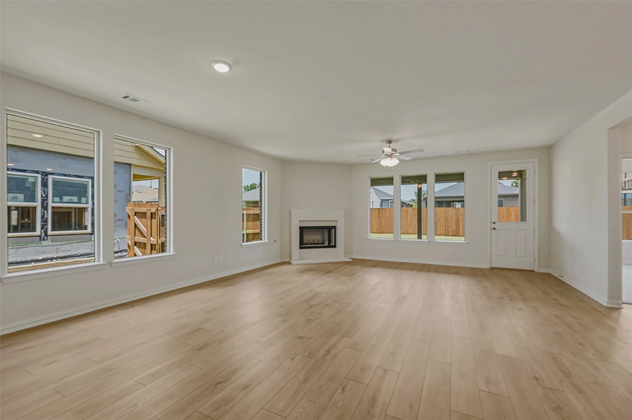Expansive living area featuring light wood-finish flooring, a contemporary fireplace with a white mantel, multiple windows, a ceiling fan, and recessed lighting