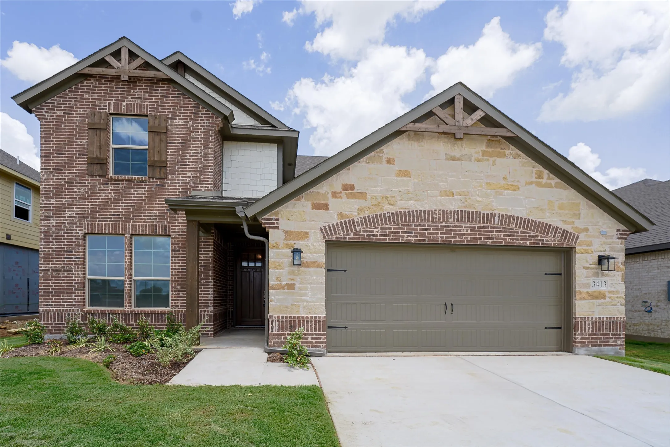 Brick and stone facade featuring a two-car garage, wood-look shutters, and decorative gable trusses
