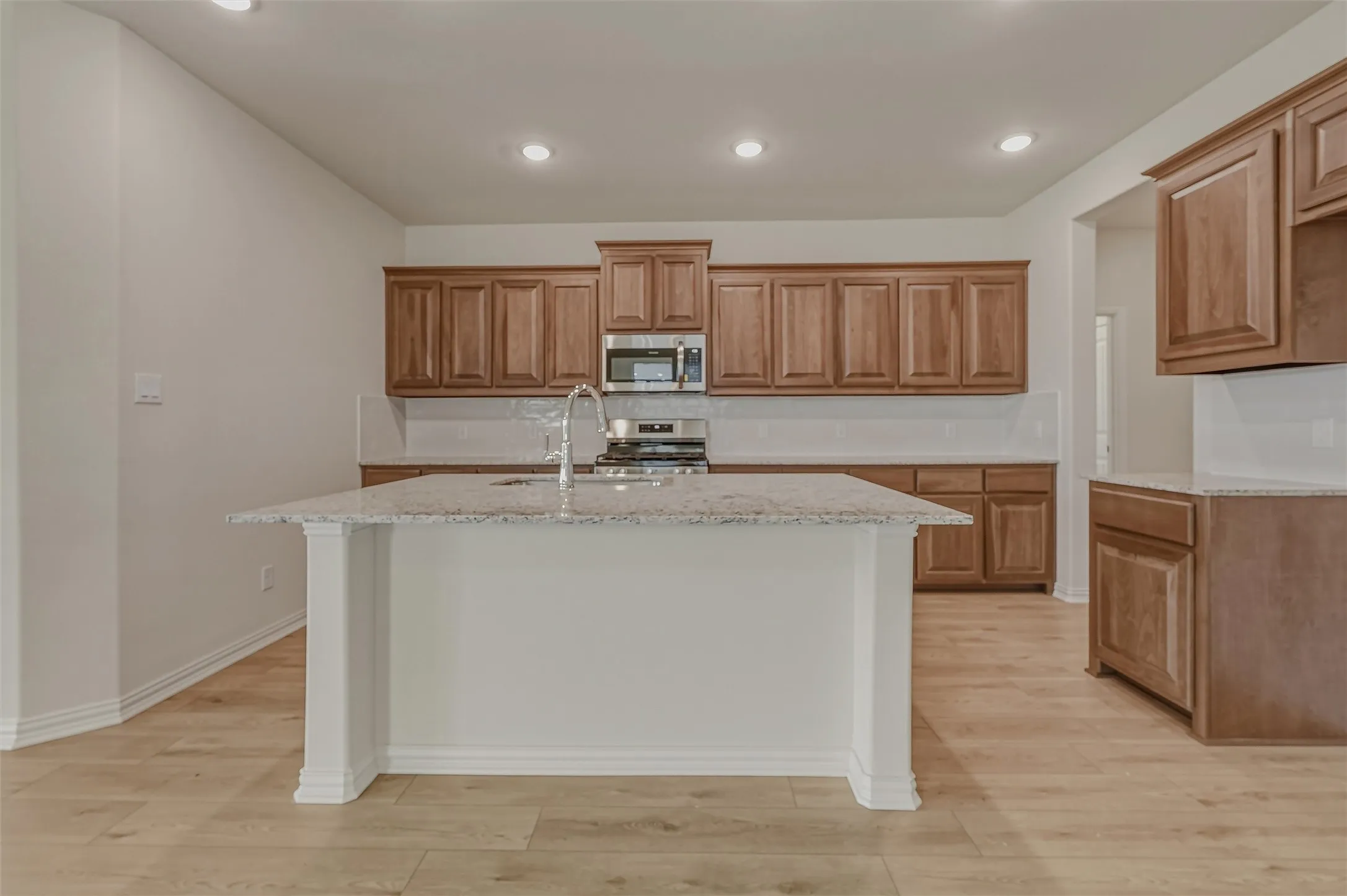 Open-concept kitchen featuring an island with a sink, light wood-finish flooring, recessed lighting, and wood cabinetry