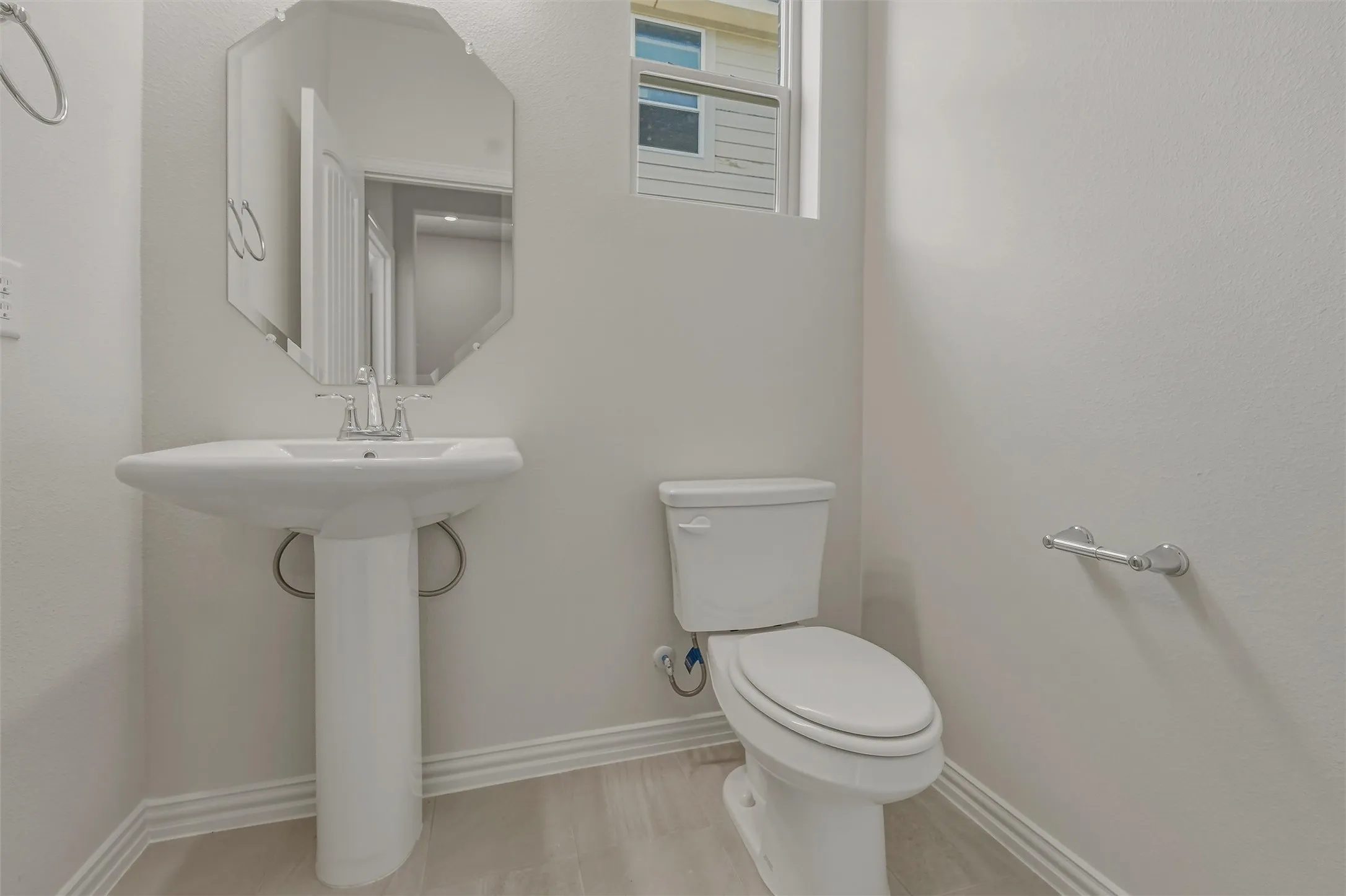 Pedestal sink with chrome faucet, octagonal mirror, and light wood-finish flooring