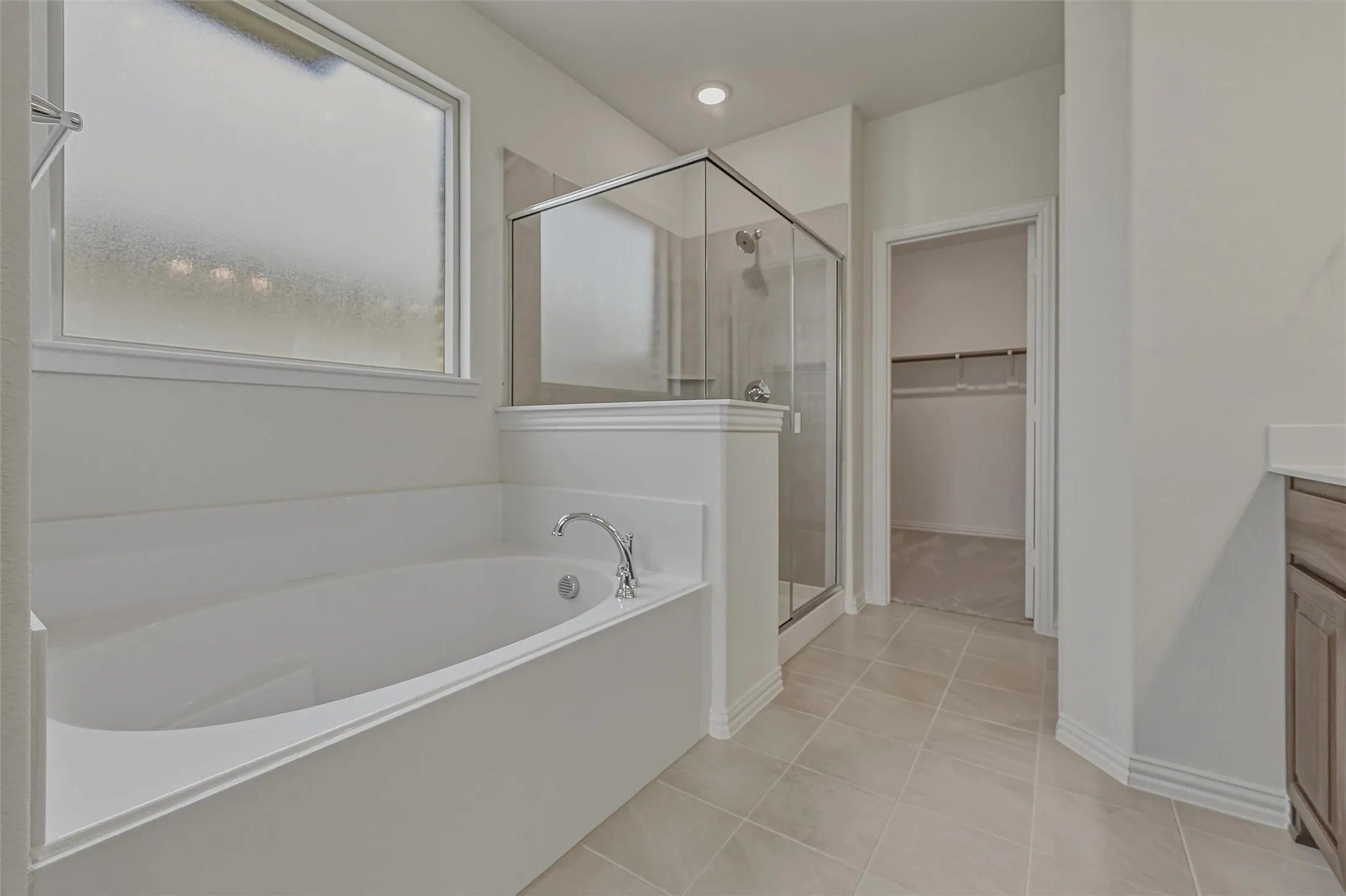 Spacious bathroom featuring an enclosed soaking tub with chrome fixtures, a glass-enclosed shower, a frosted window, and large format tile flooring