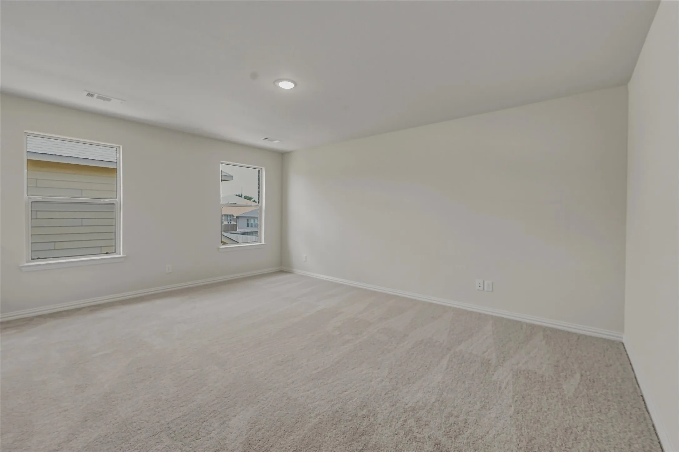 Spacious room featuring neutral carpeting, two windows with white trim, recessed lighting, and light-toned walls