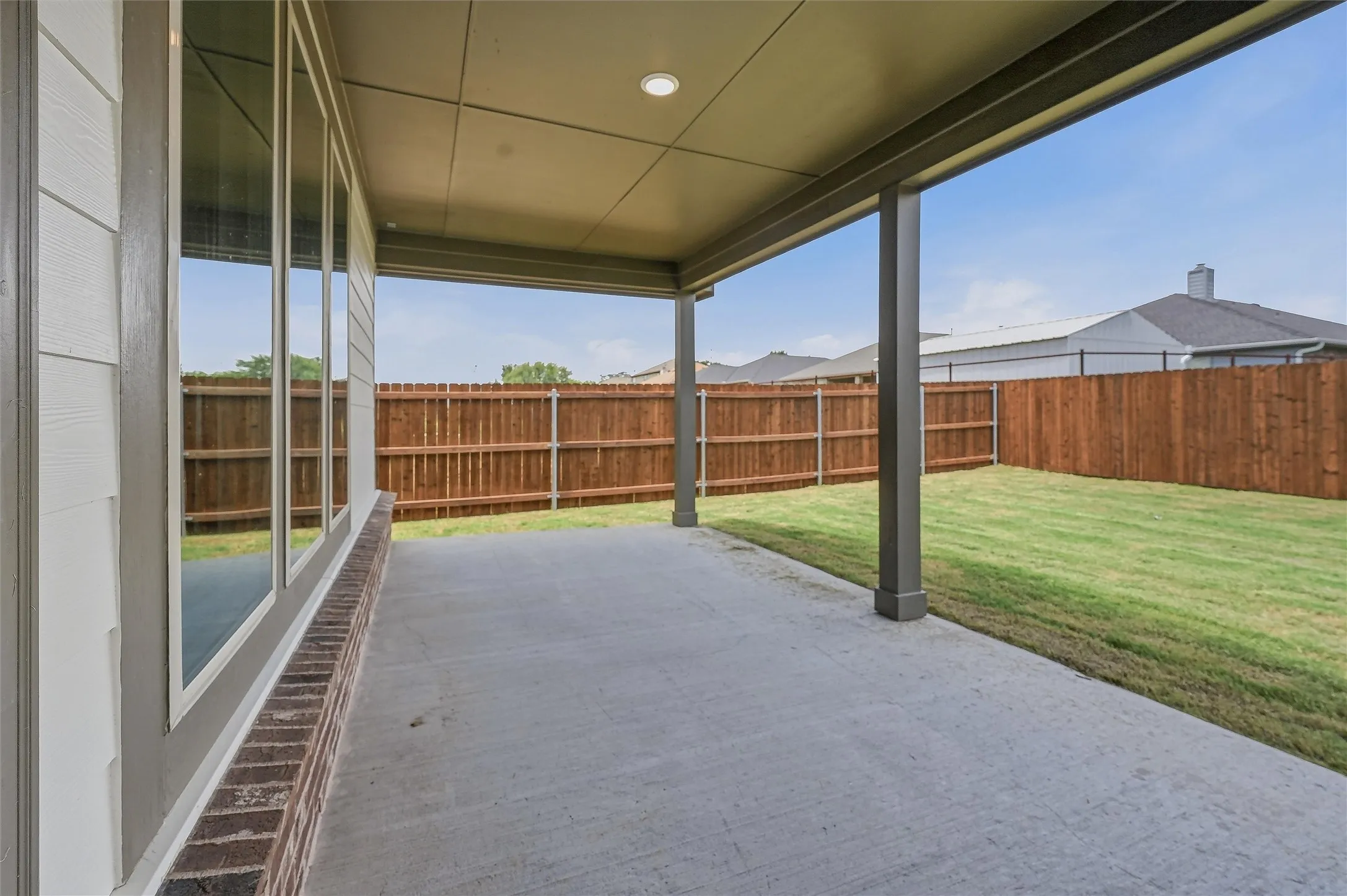 Covered concrete patio extending to a fenced backyard with grass lawn