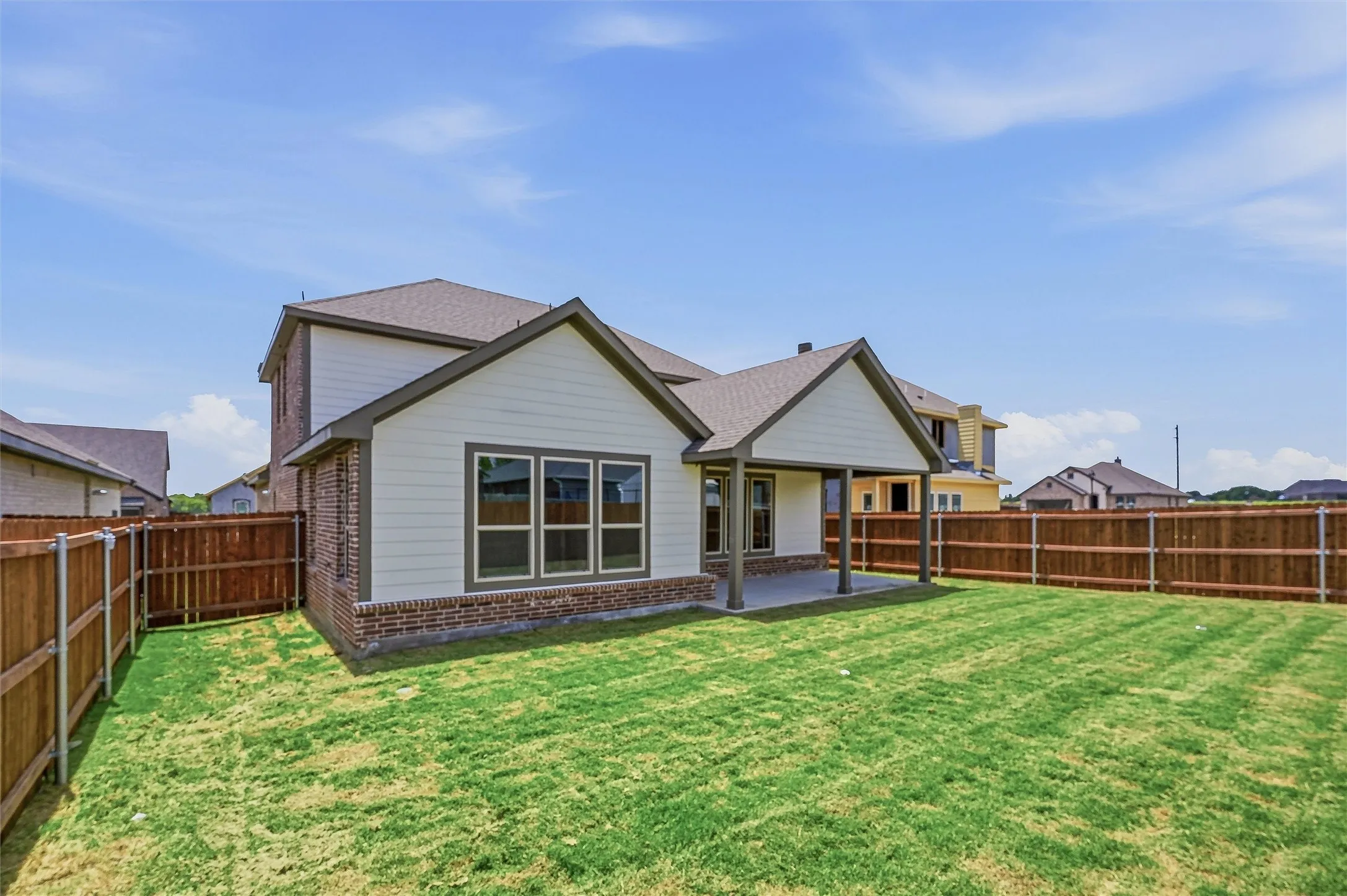 Expansive fenced backyard featuring a manicured lawn, a covered patio, and a brick and siding exterior
