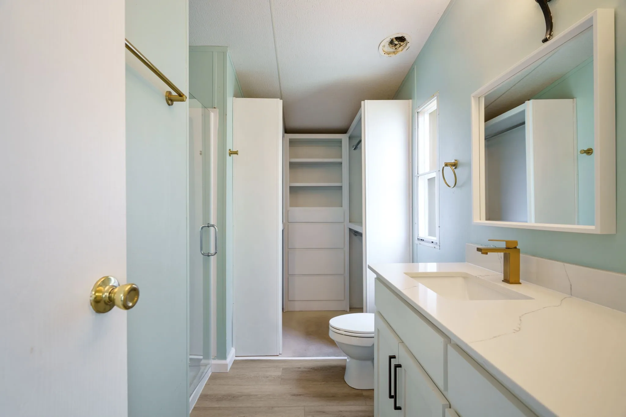 Bathroom with light blue walls featuring a white vanity with an integrated sink, gold-finish faucet, and coordinating door hardware