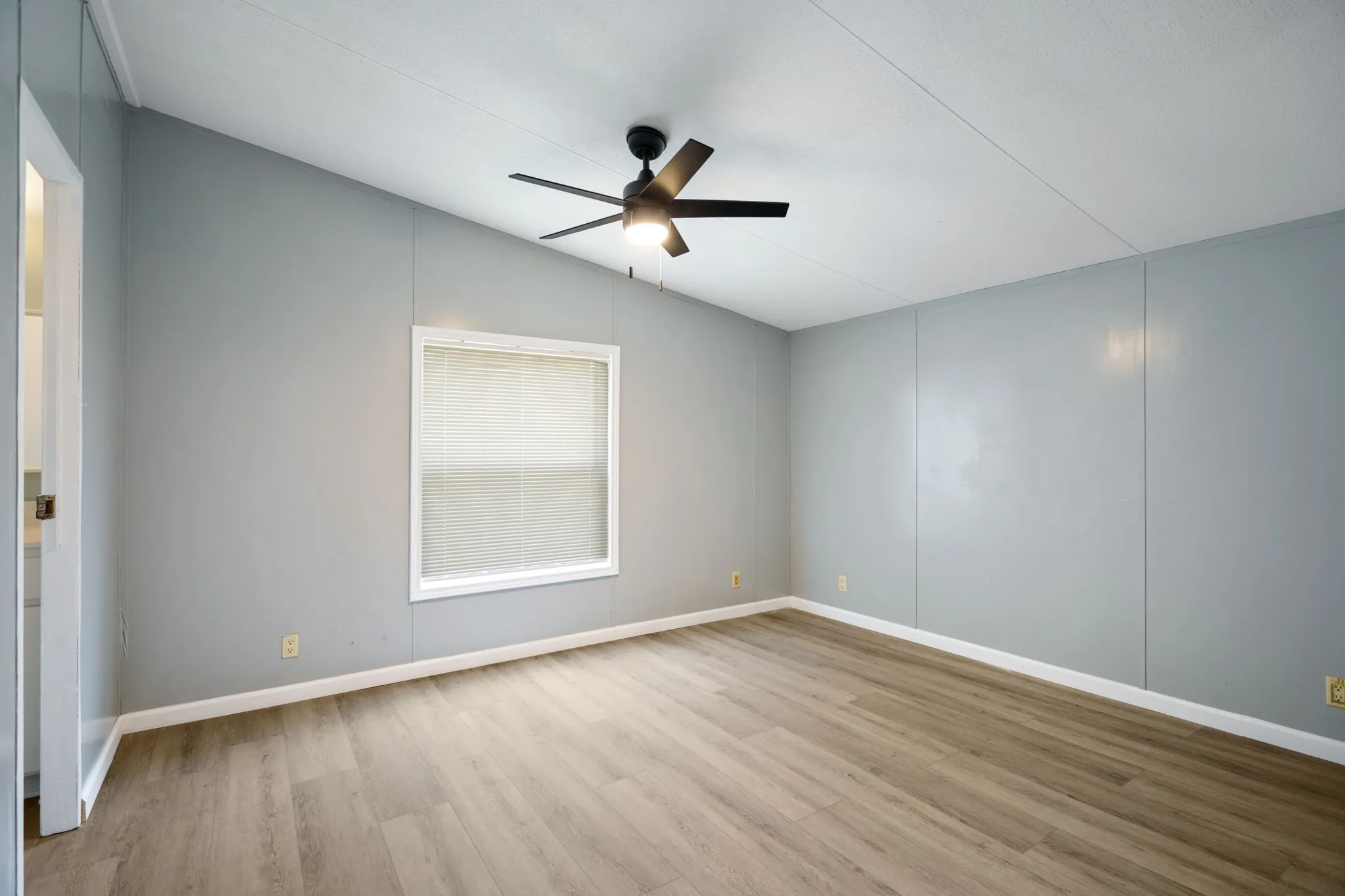 Spacious room featuring wood-finish flooring, light gray walls, and a vaulted ceiling
