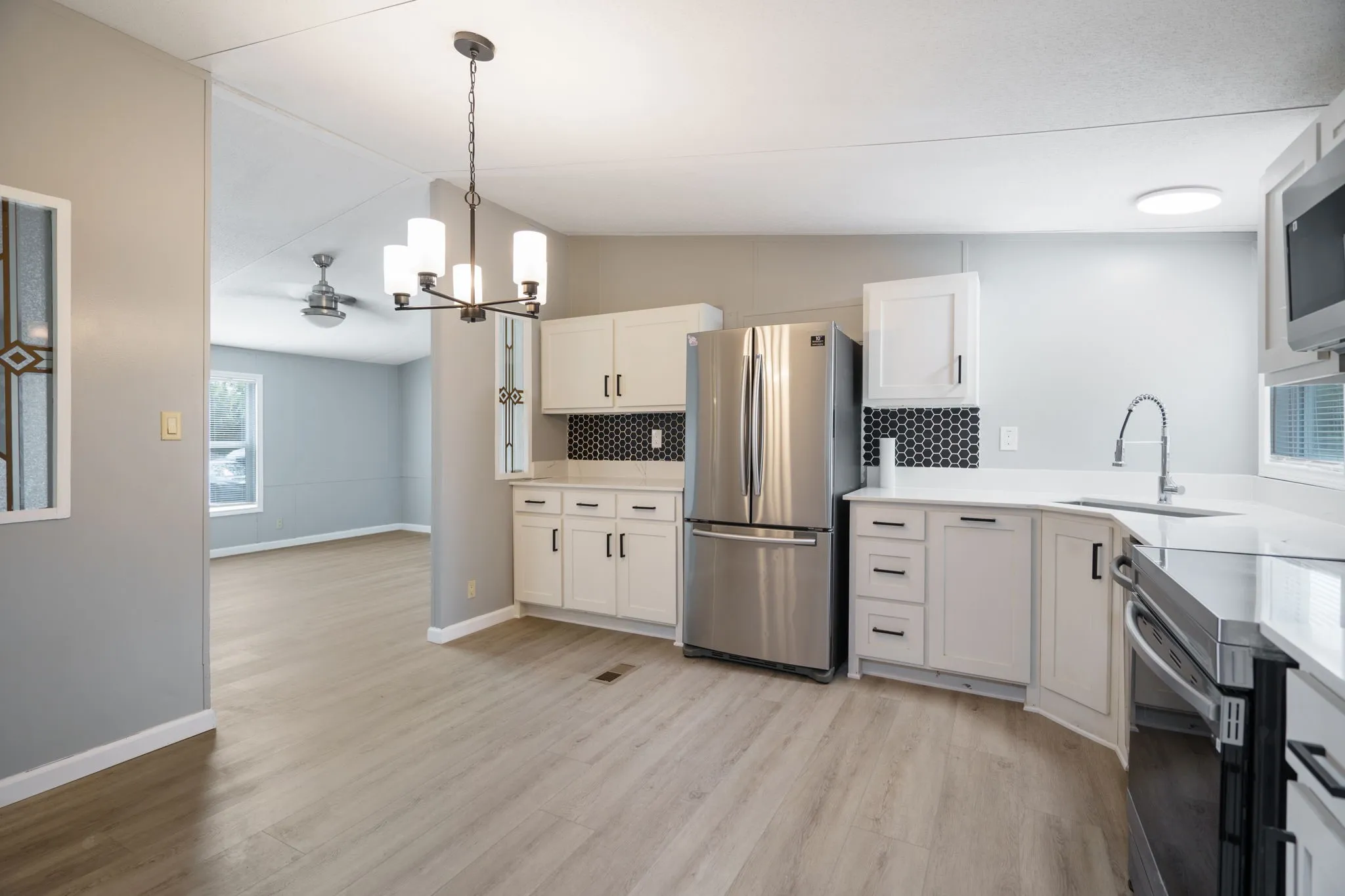 Modern kitchen featuring white cabinetry, stainless steel appliances, a black honeycomb tile backsplash, and light wood-finish flooring