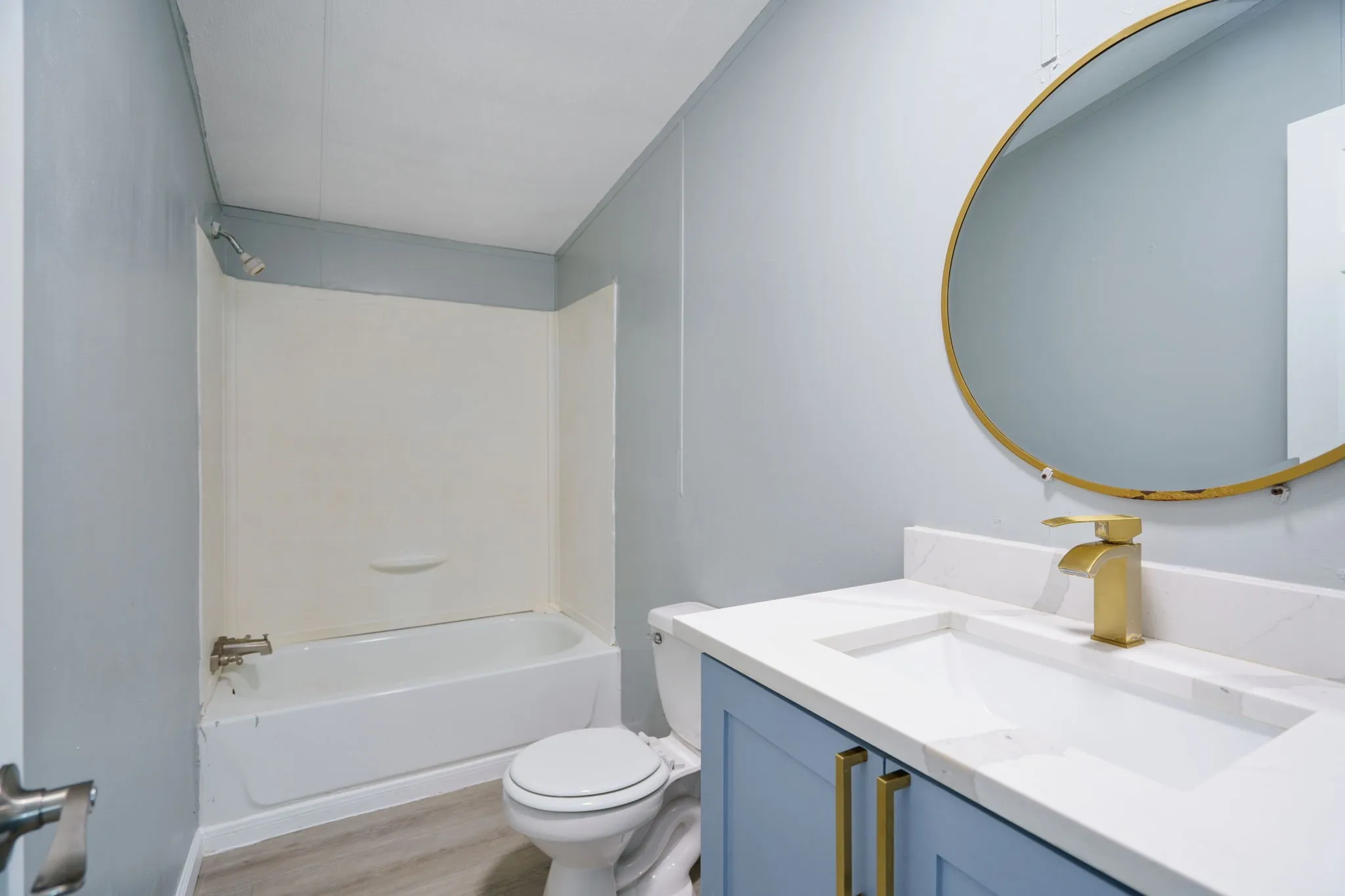 Bathroom featuring a white bathtub, a toilet, a vanity with a white countertop and integrated sink, a gold-finish faucet, and a round gold-framed mirror