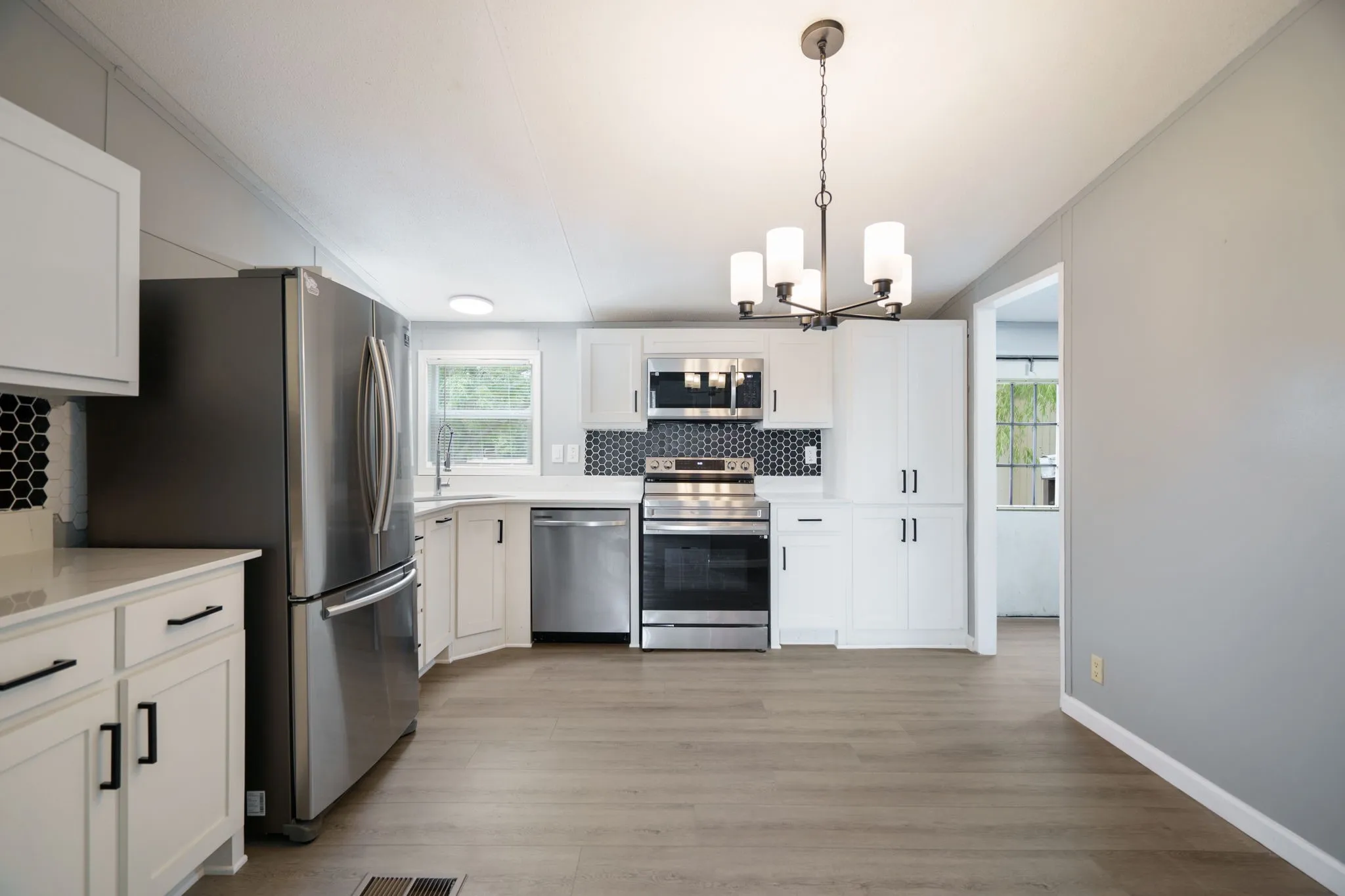 Kitchen featuring stainless steel appliances, white cabinetry with matte black hardware, hexagon tile backsplash, and wood-finish flooring