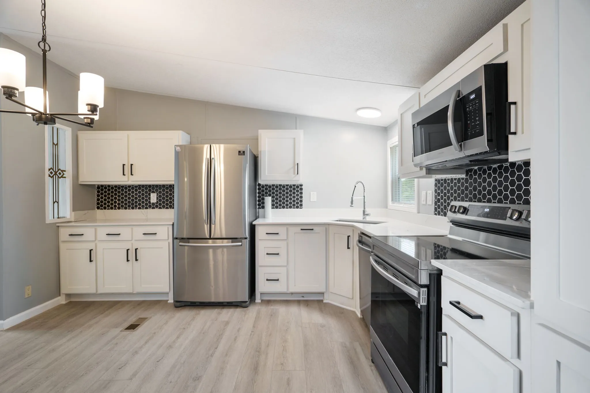 Kitchen featuring white cabinetry, black hexagonal tile backsplash, stainless steel appliances, light countertops, and wood-finish flooring
