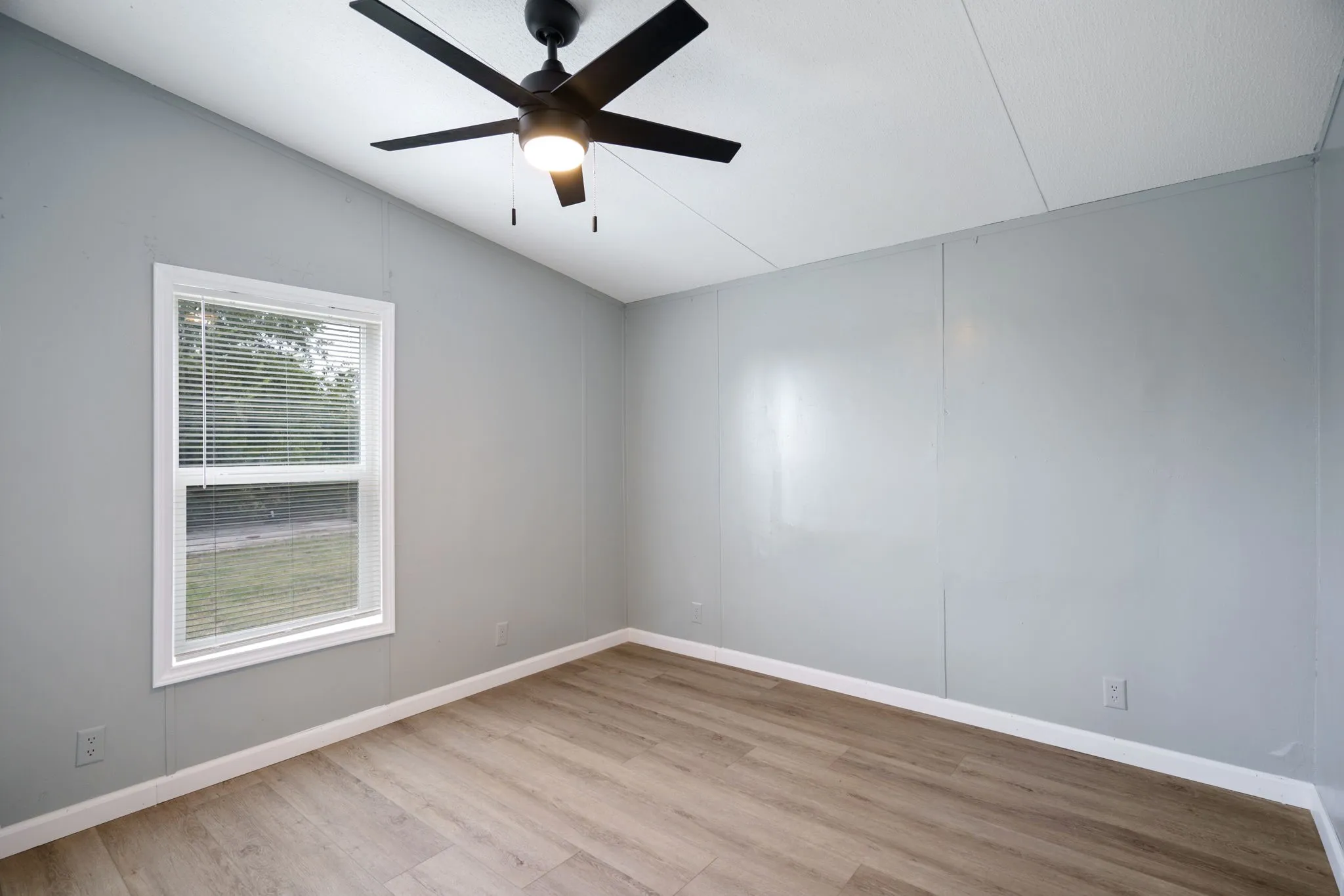 Room featuring wood-finish flooring, a window with blinds, and white baseboards
