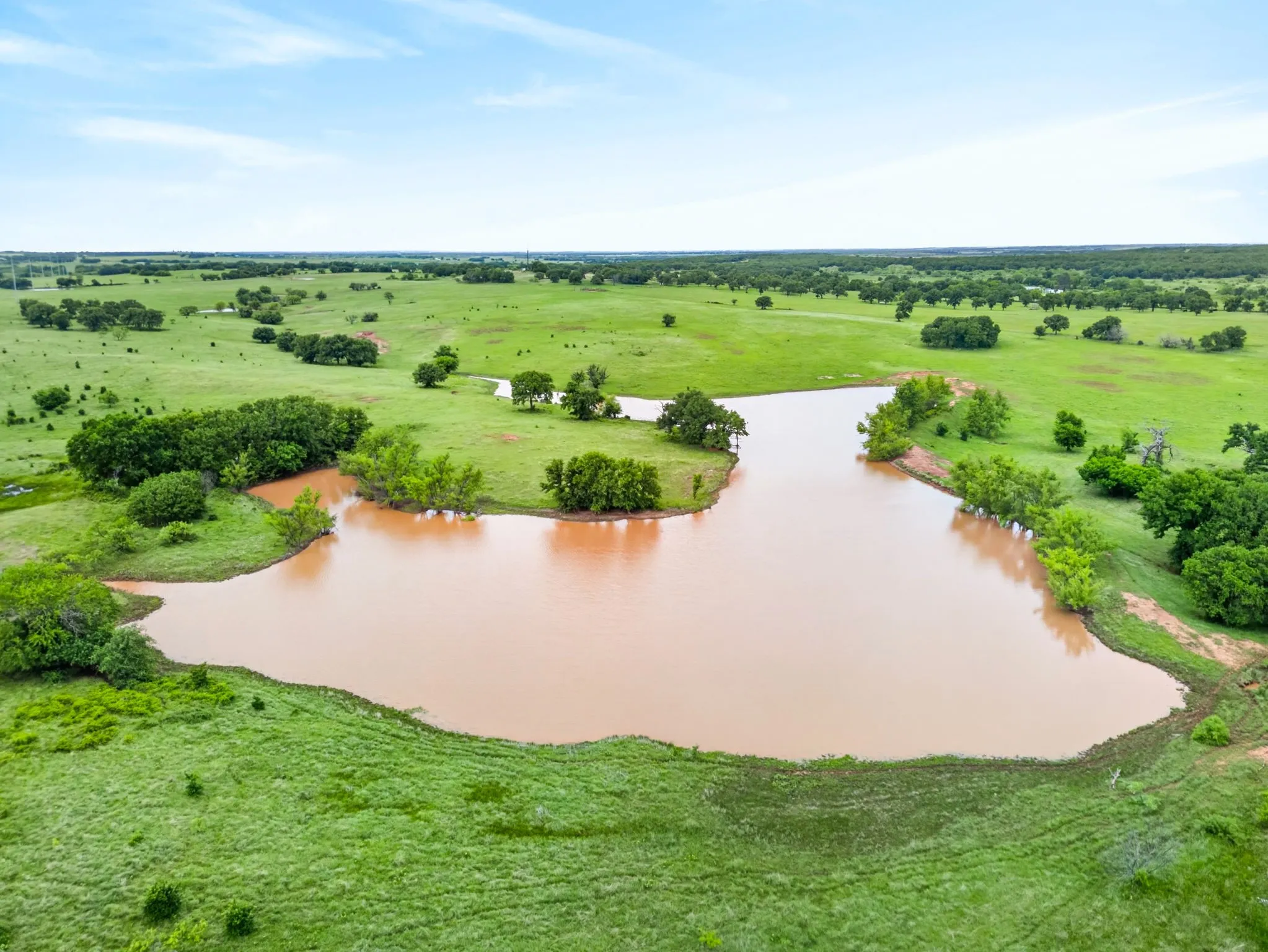 Expansive body of water surrounded by lush green pastures and scattered trees