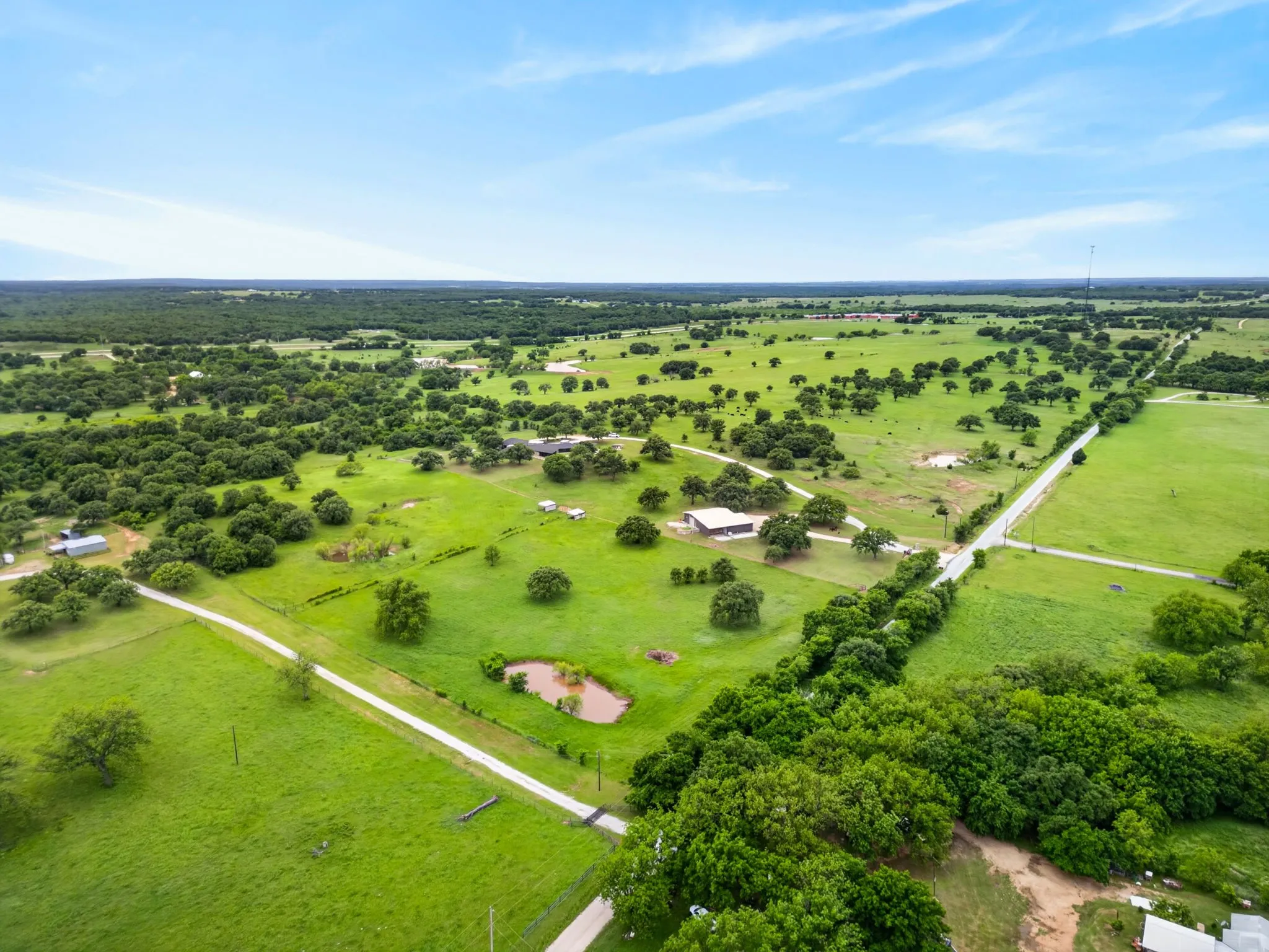 Expansive property featuring verdant pastures, scattered mature trees, and a visible pond