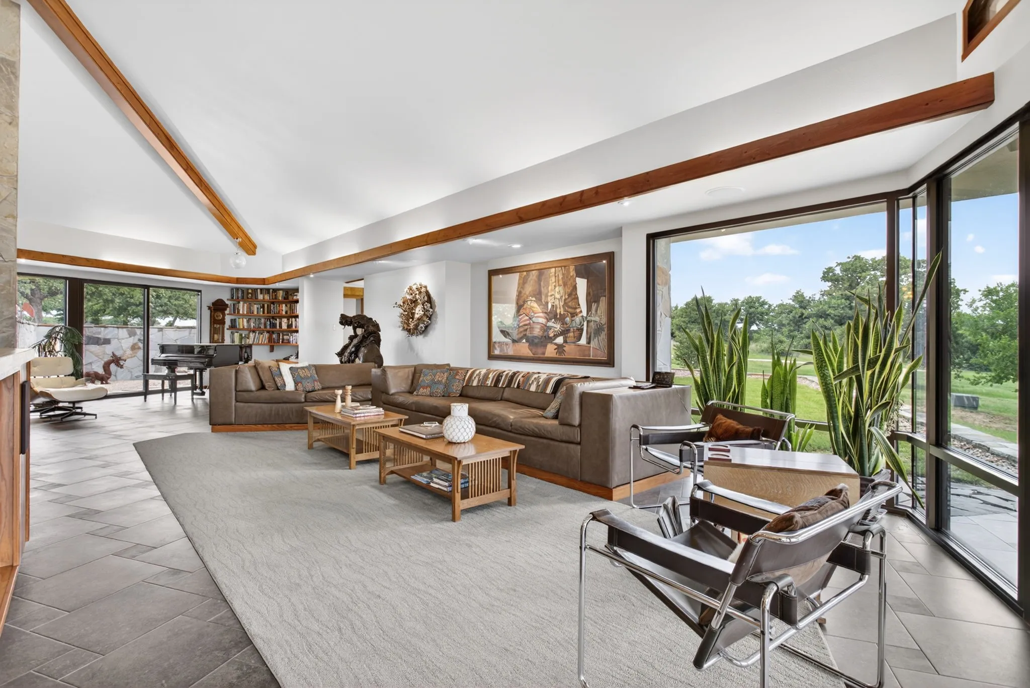 Spacious living area featuring a vaulted ceiling with exposed wood beams, expansive floor-to-ceiling windows, and large format tile flooring