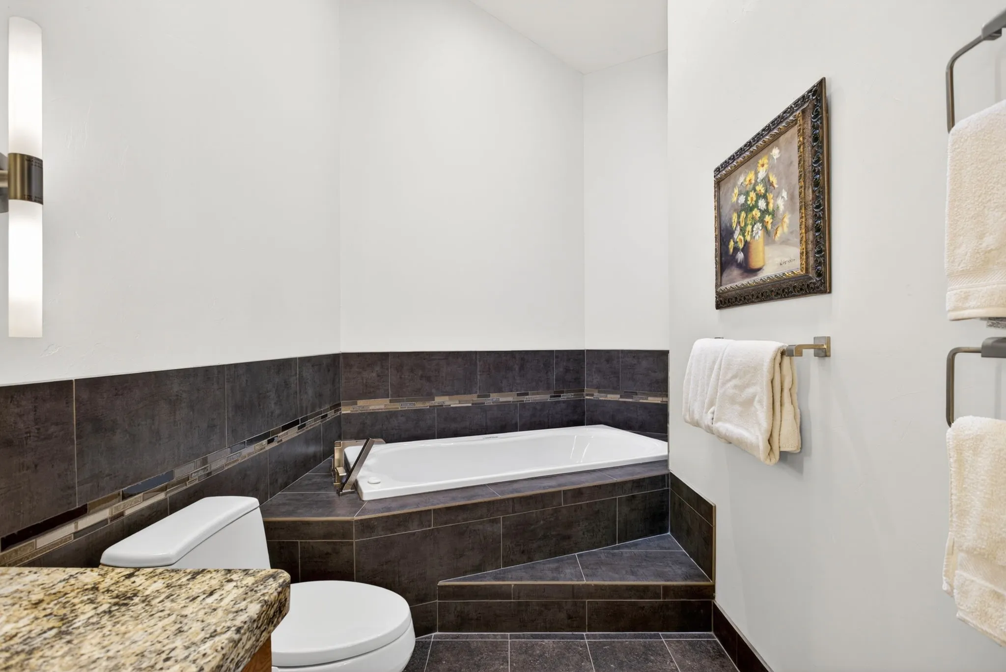 Corner soaking tub set within dark tile surround with decorative accent band