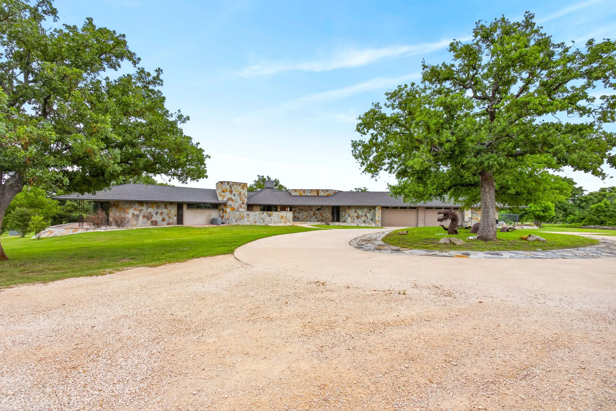 Ranch-style residence featuring a natural stone exterior, a gravel driveway, and a circular stone-edged island