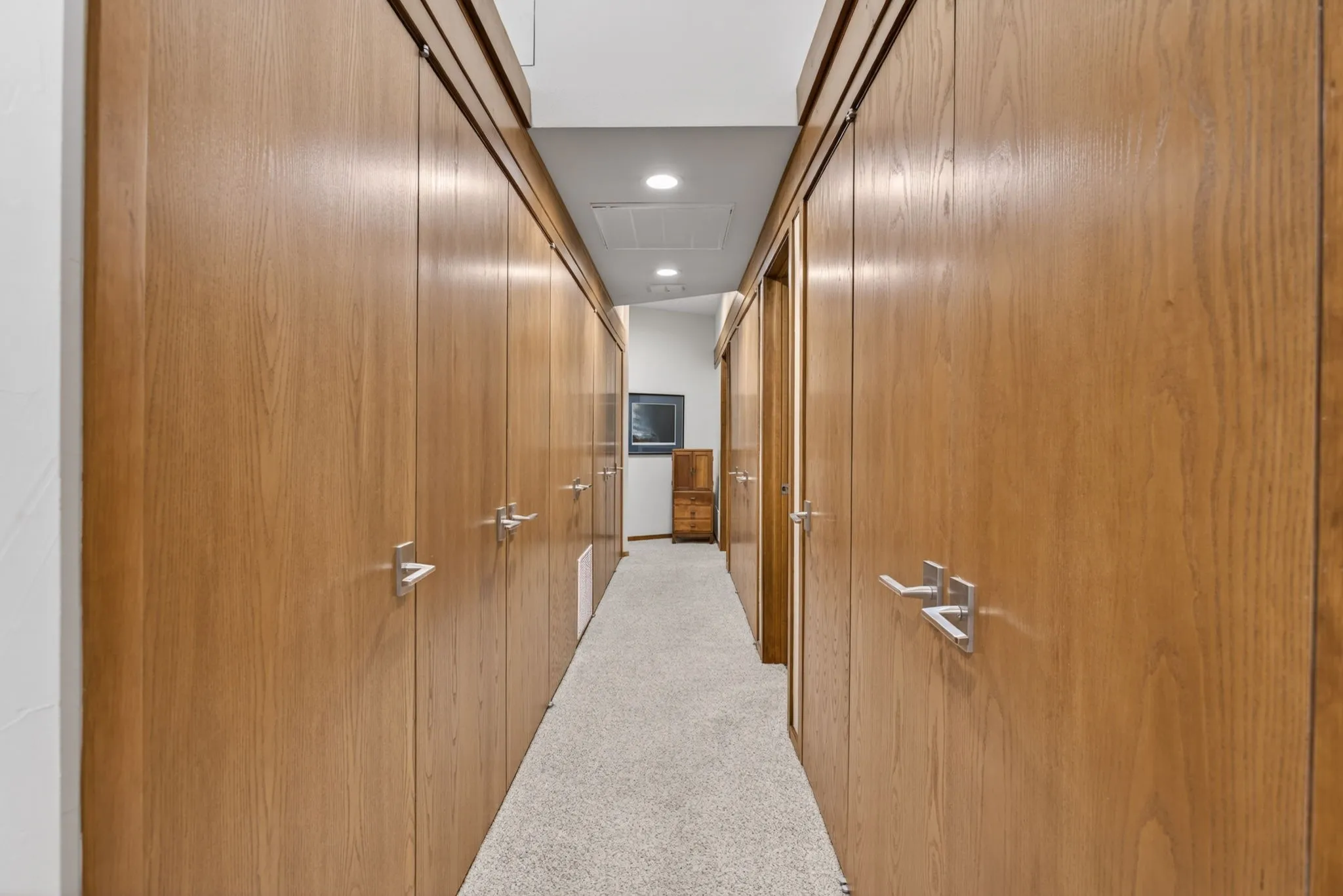 Hallway featuring extensive wood-finish cabinetry with brushed nickel hardware, recessed ceiling lighting, and light-toned carpet flooring