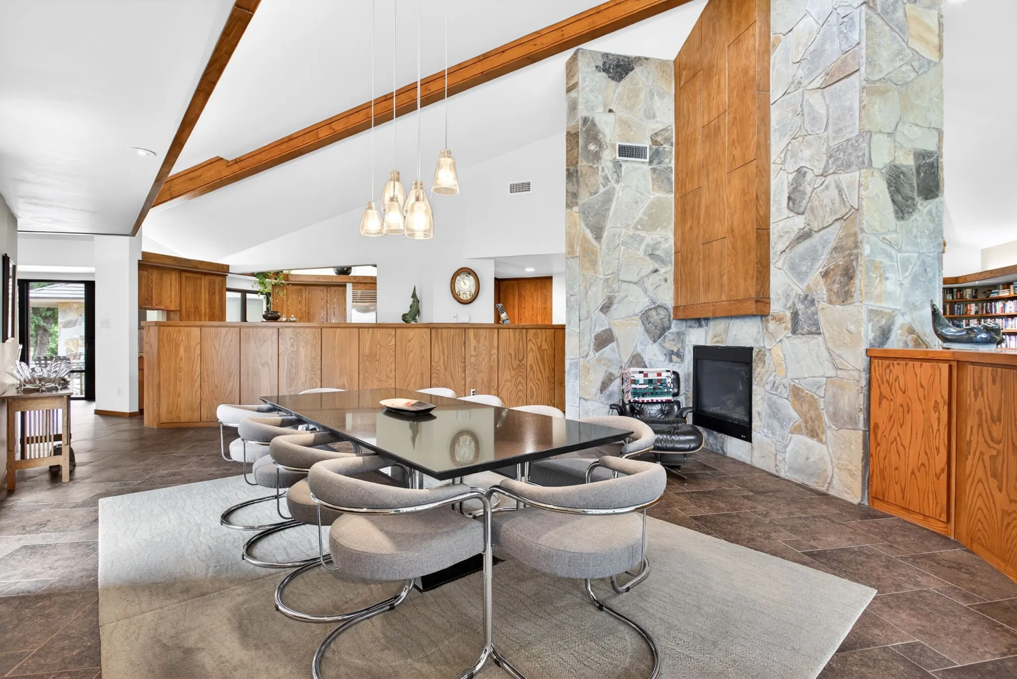 Dining area featuring a vaulted ceiling with exposed wood beams, a stone-clad fireplace, and tile flooring