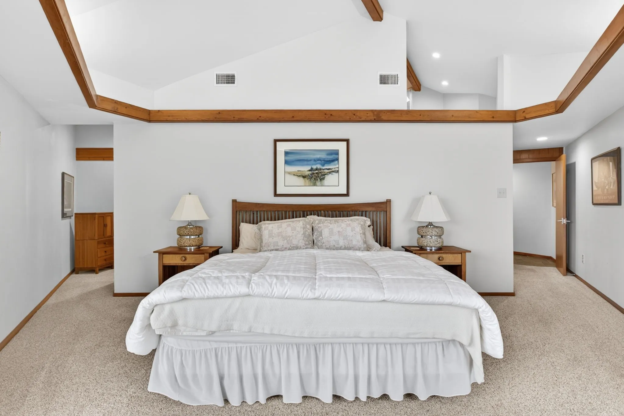 Spacious bedroom featuring vaulted ceilings with exposed wood beams, light-toned carpeting, and recessed lighting
