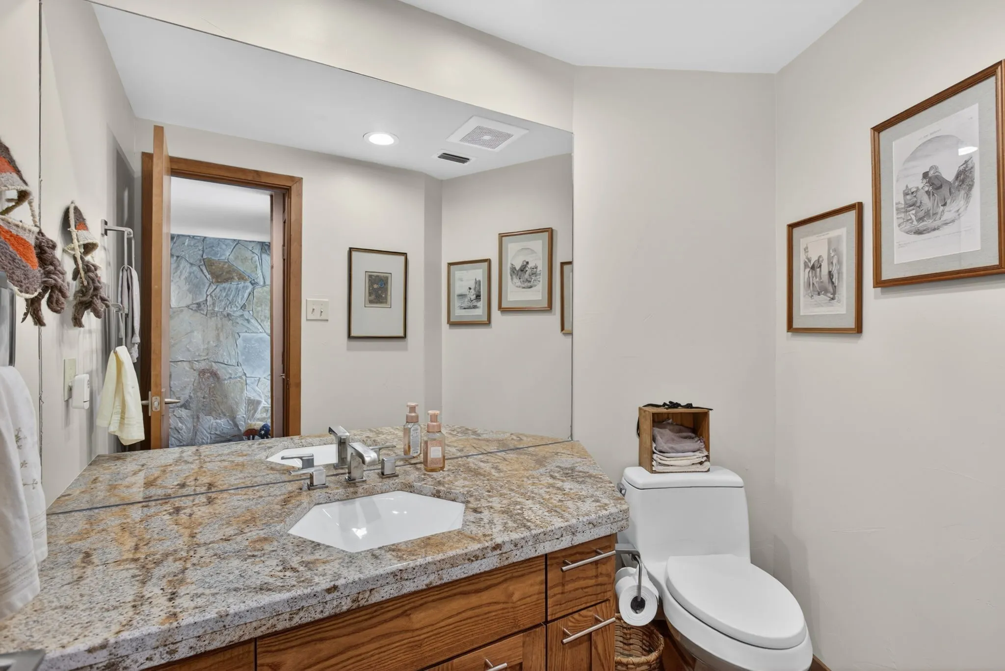 Front Half Bathroom with a granite-style countertop, integrated white sink, chrome faucet, wood-finish vanity, and a full-width mirror