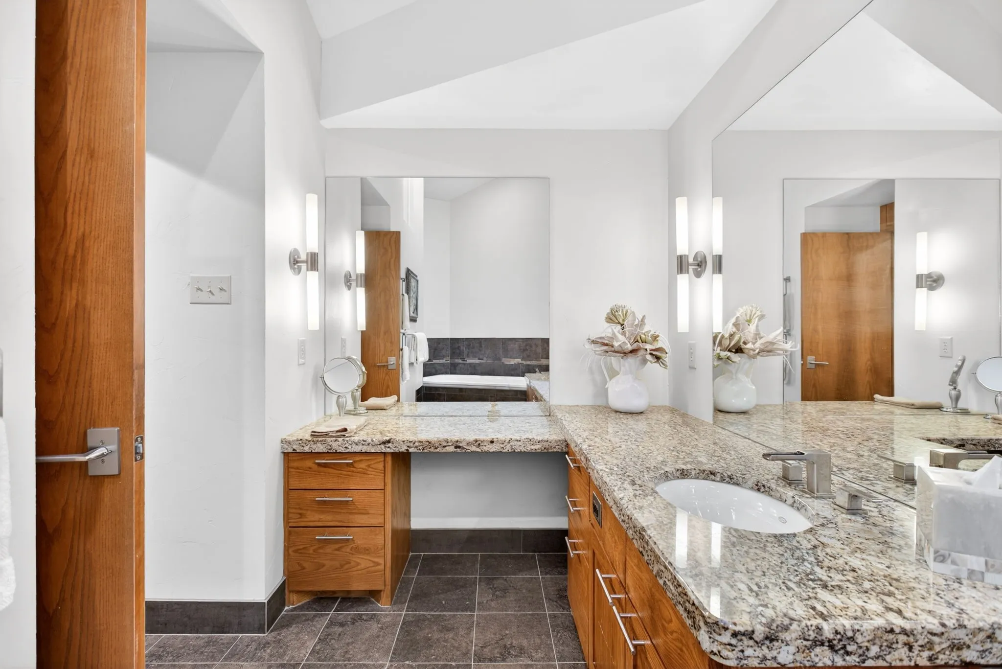 Spacious bathroom featuring dual granite-finish countertops with integrated sinks, rich wood cabinetry, and a dedicated vanity area