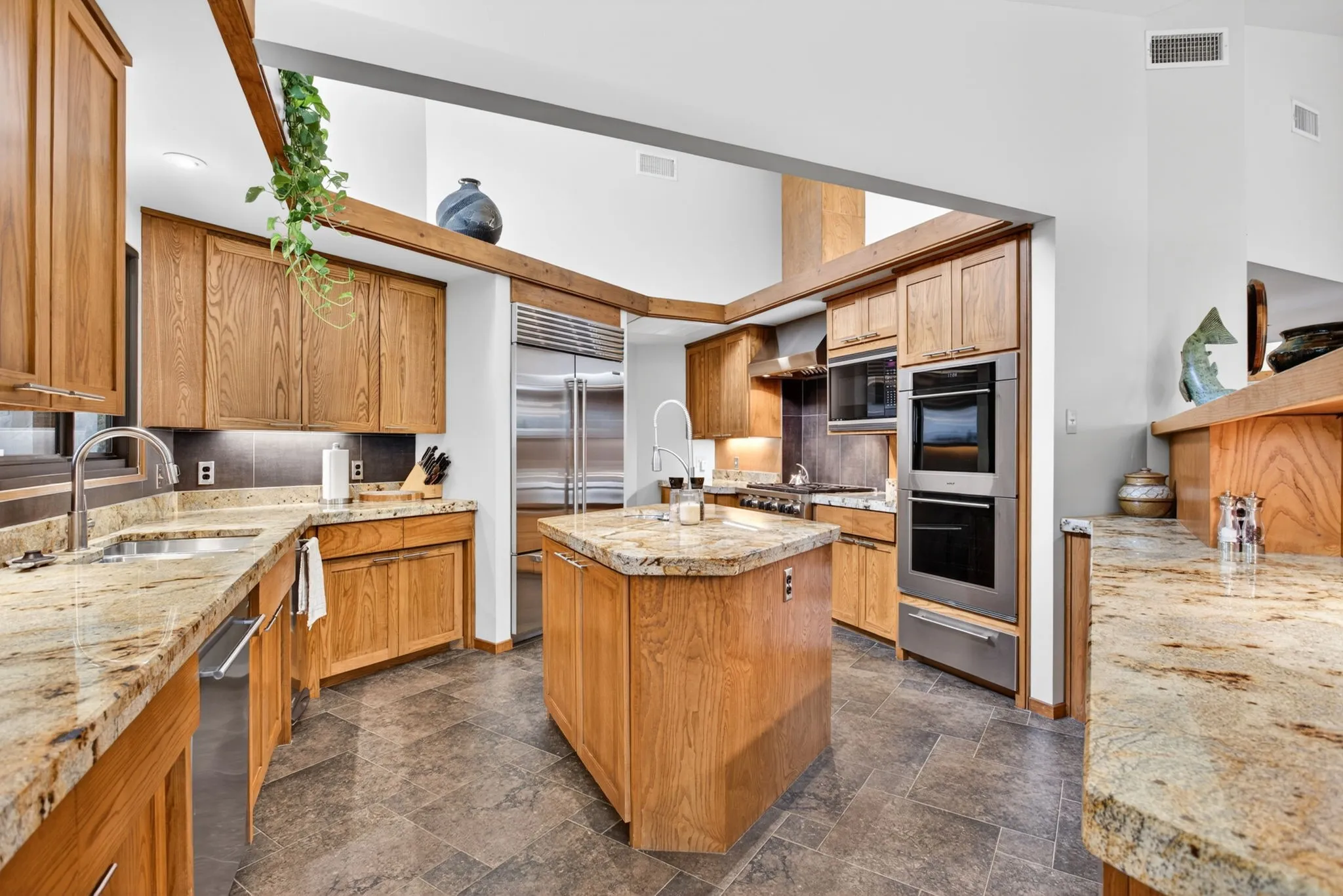 Kitchen featuring wood cabinetry, stainless steel appliances, stone countertops, a central island, and tile flooring