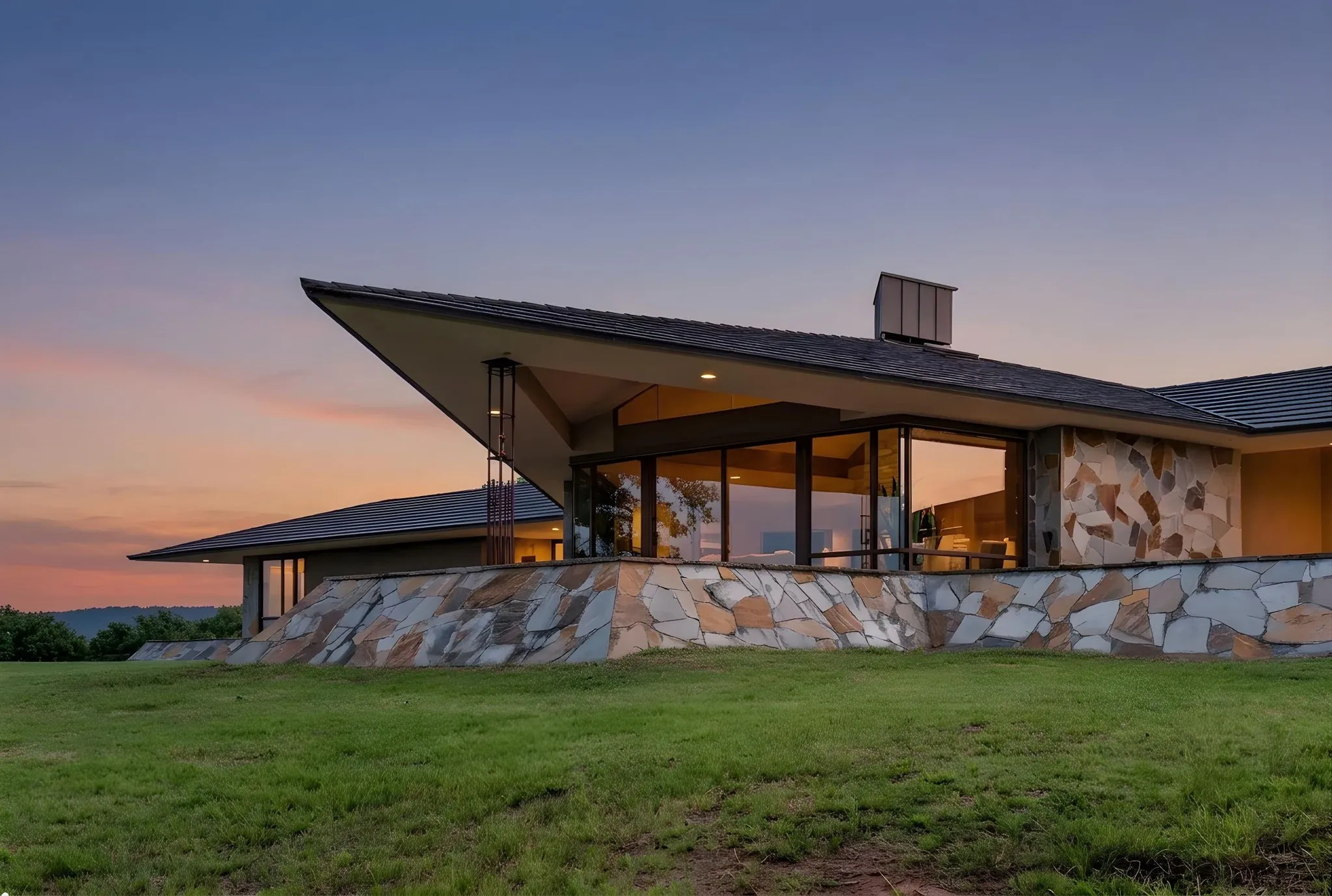 Modern architectural residence featuring extensive stone veneer, a distinctive cantilevered roofline, large picture windows, and a chimney stack