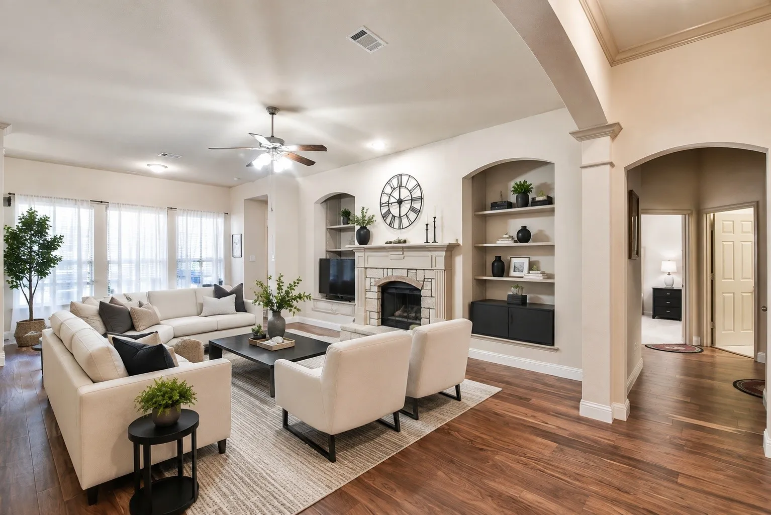 Wood-finish flooring, recessed lighting, ceiling fan, stone-surround fireplace with hearth, and built-in shelving with arched alcoves