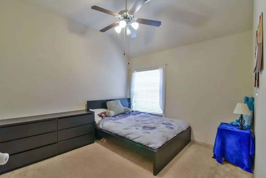 Bedroom with vaulted ceiling, ceiling fan with light fixture, window with blinds, and neutral carpet flooring