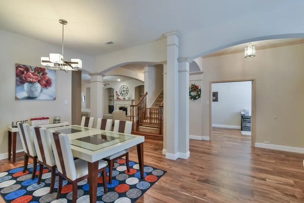 Dining area with wood-finish flooring, featuring a contemporary chandelier and arched doorways