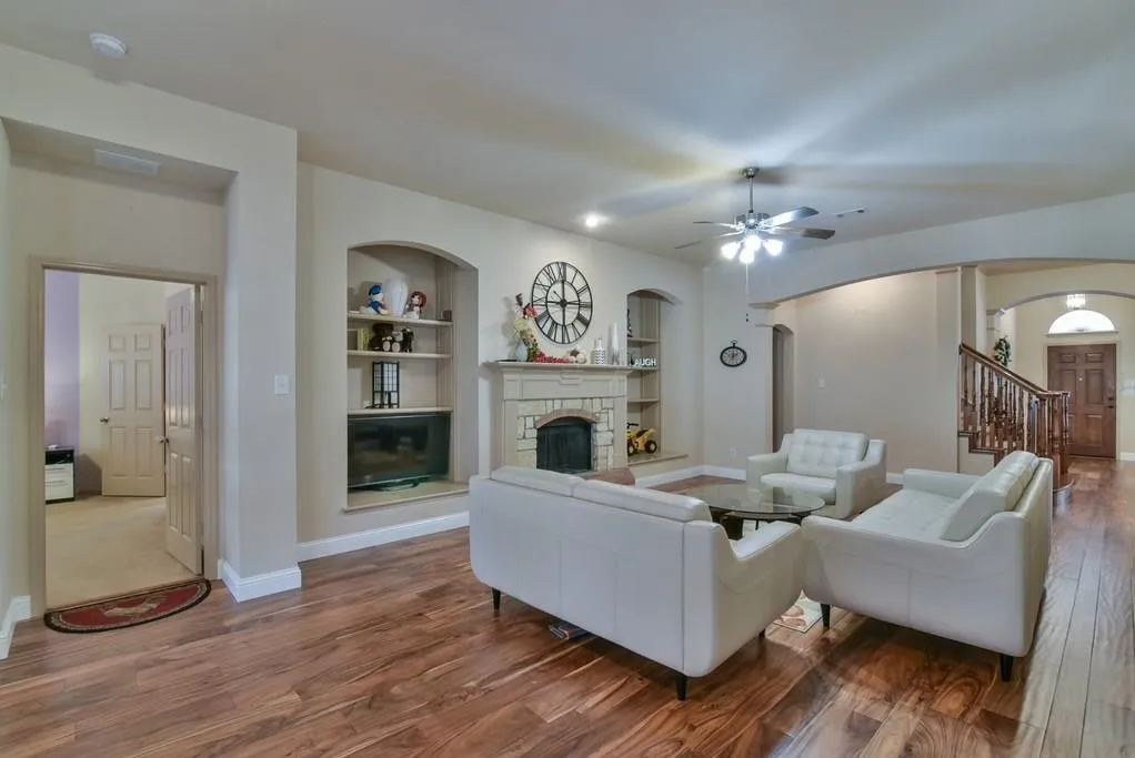 Spacious living area featuring wood-finish flooring, a stone fireplace, and built-in shelving