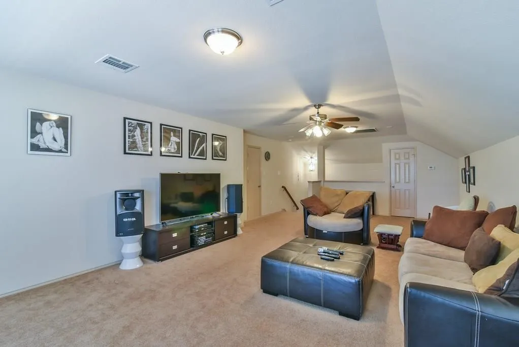 Carpeted recreation room featuring vaulted ceilings, a ceiling fan with integrated lighting, and a built-in media console