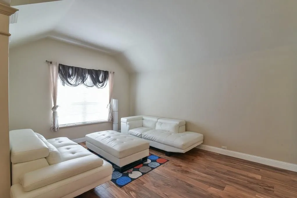 Vaulted ceiling room featuring wood-finish flooring, a window with horizontal blinds, and neutral wall tones